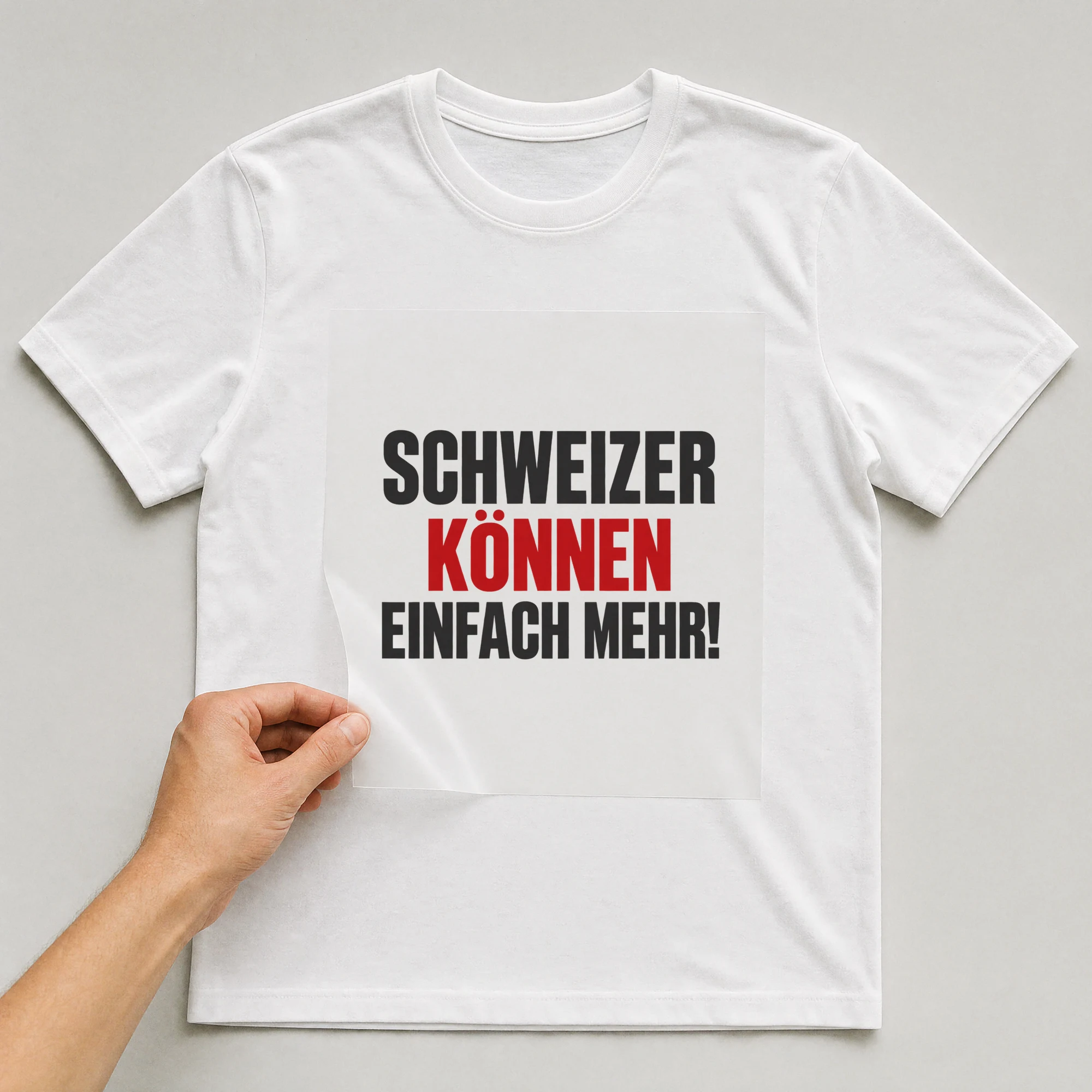 Bügelbild „Schweizer können einfach mehr!“ auf weißem T-Shirt, Folie wird aufgelegt