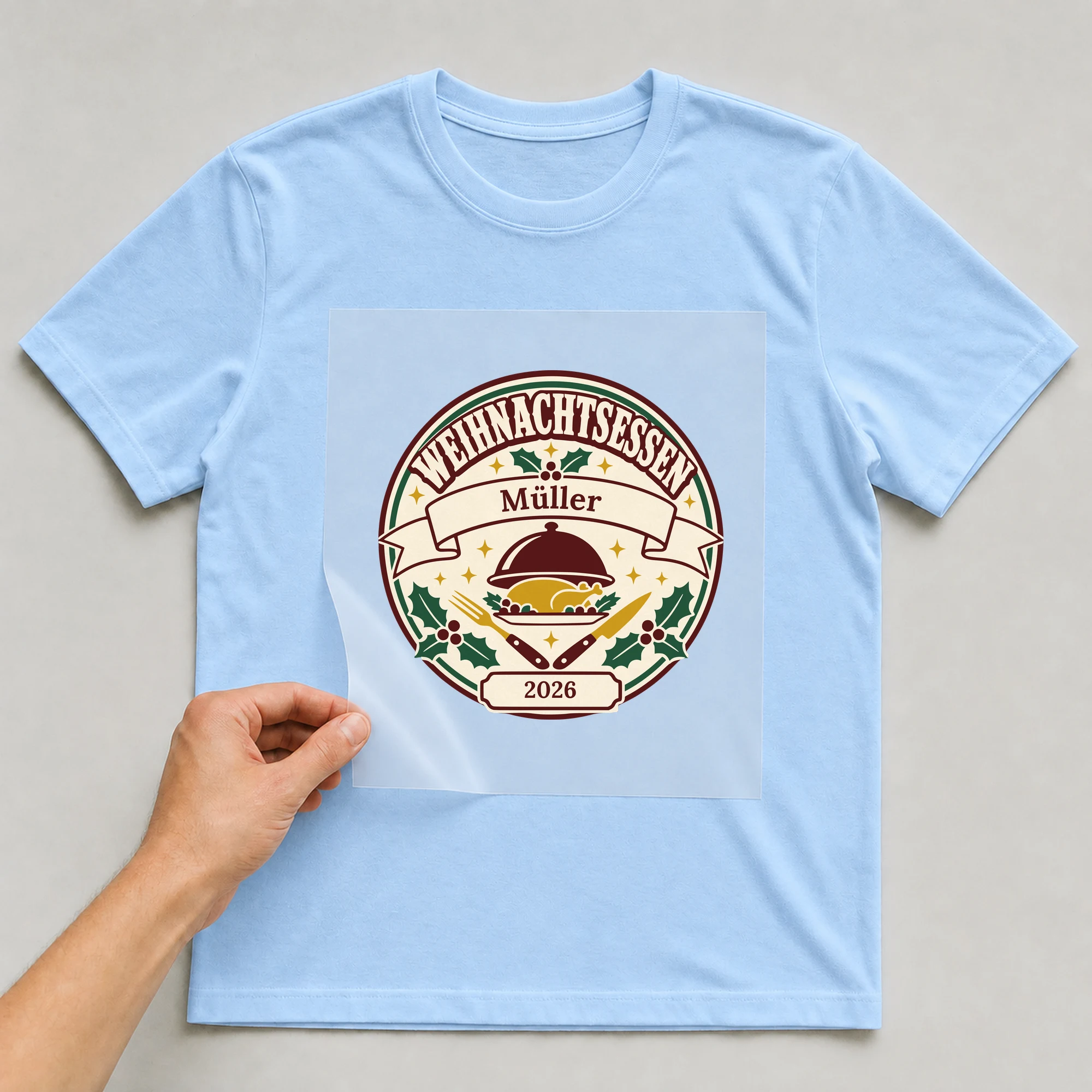 Bügelbild Weihnachtsessen mit Nachname und Jahr auf hellblauem T-Shirt, Folie wird aufgelegt