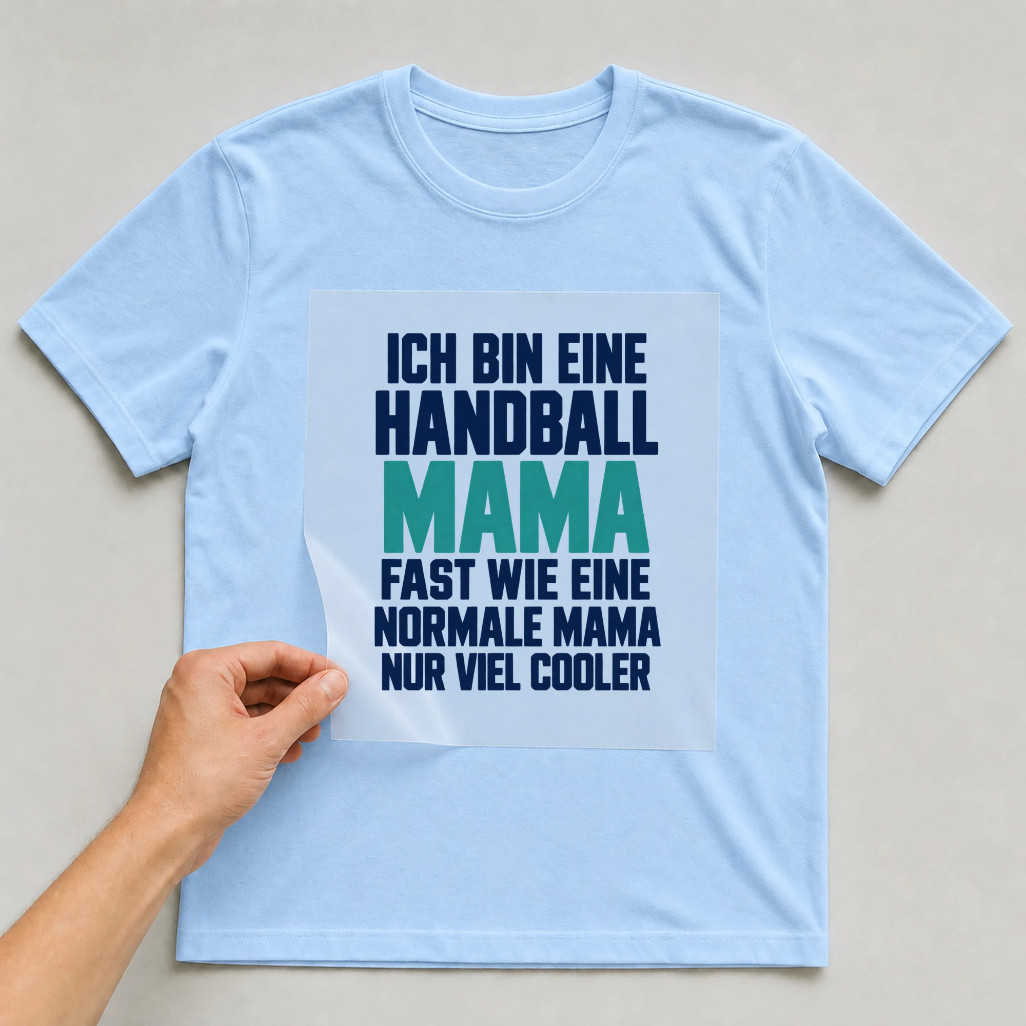 Bügelbild „Ich bin eine Handball Mama fast wie eine normale Mama nur viel cooler“ auf babyblauem T-Shirt, Folie wird aufgelegt