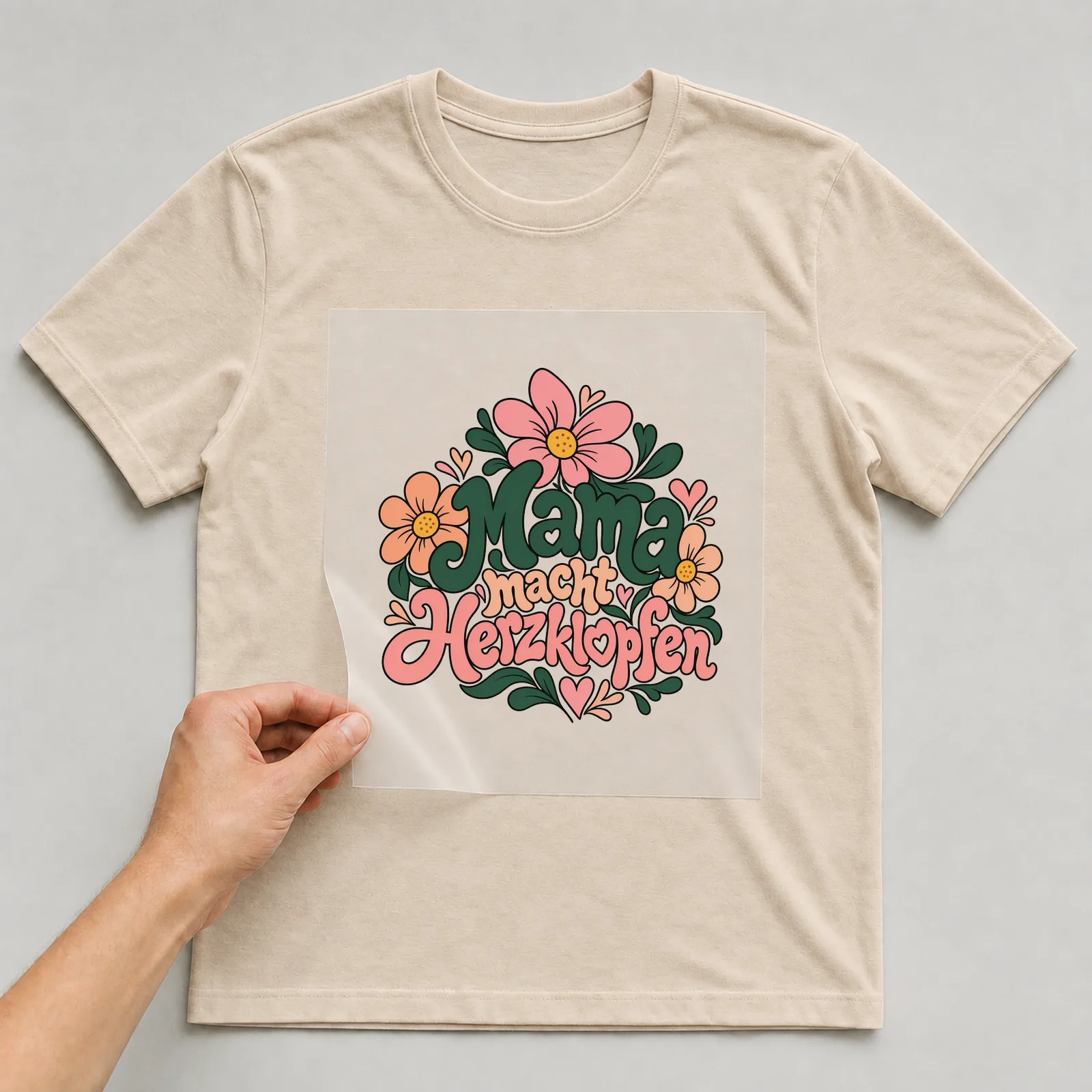 Bügelbild „Mama macht Herzklopfen“ auf beigem T-Shirt, Folie wird aufgelegt