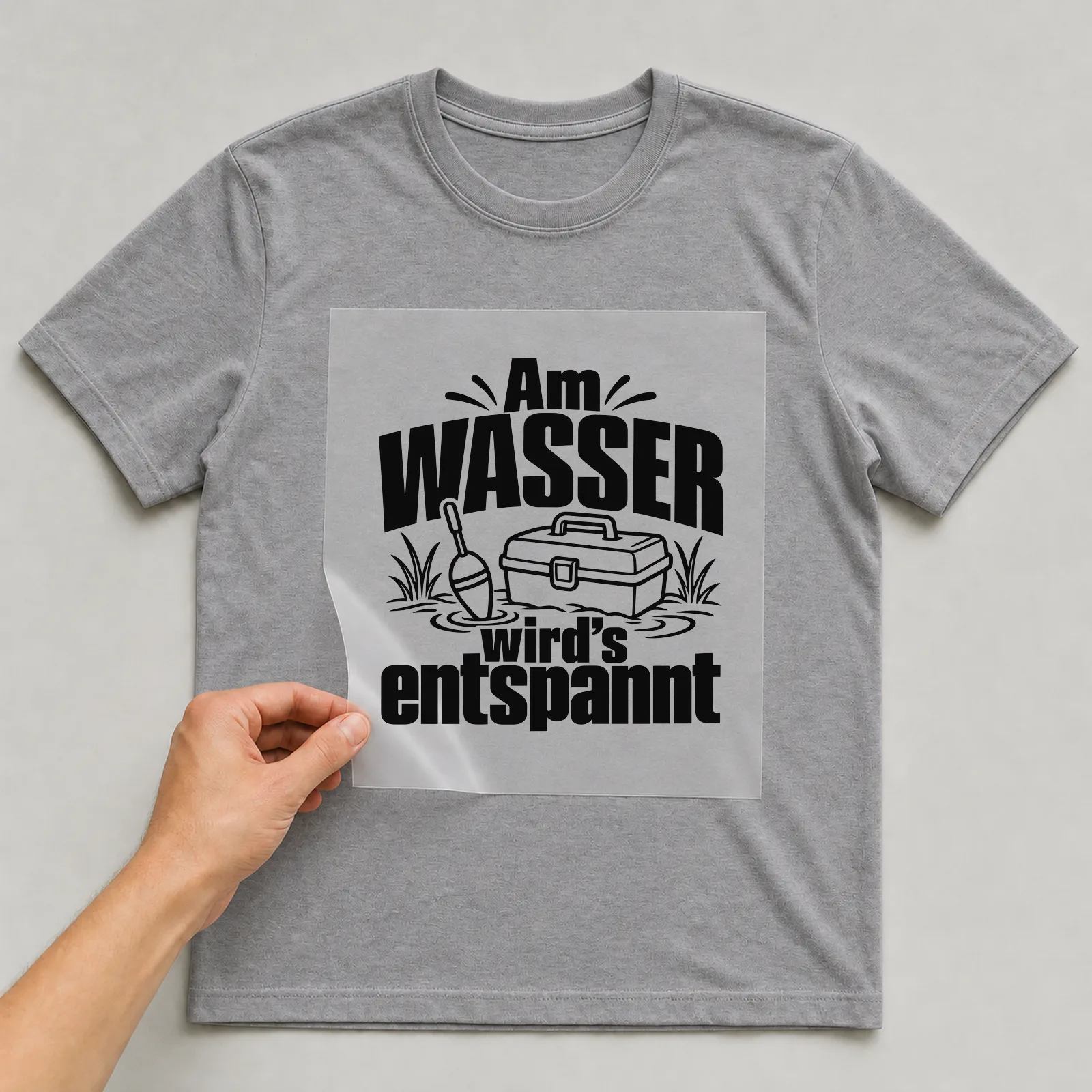 Bügelbild „Am Wasser wird’s entspannt“ auf grauem T-Shirt, Folie wird aufgelegt