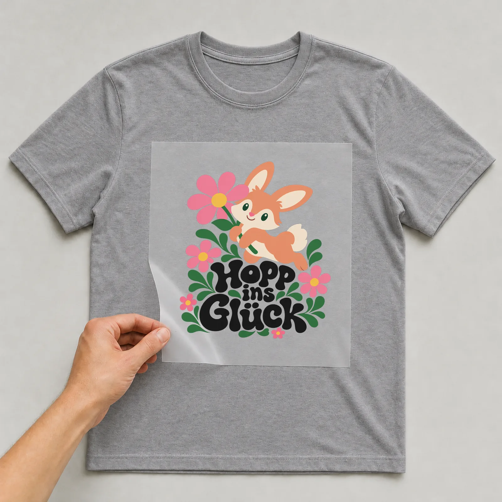 Bügelbild „Hopp ins Glück“ auf grauem T-Shirt, Folie wird aufgelegt