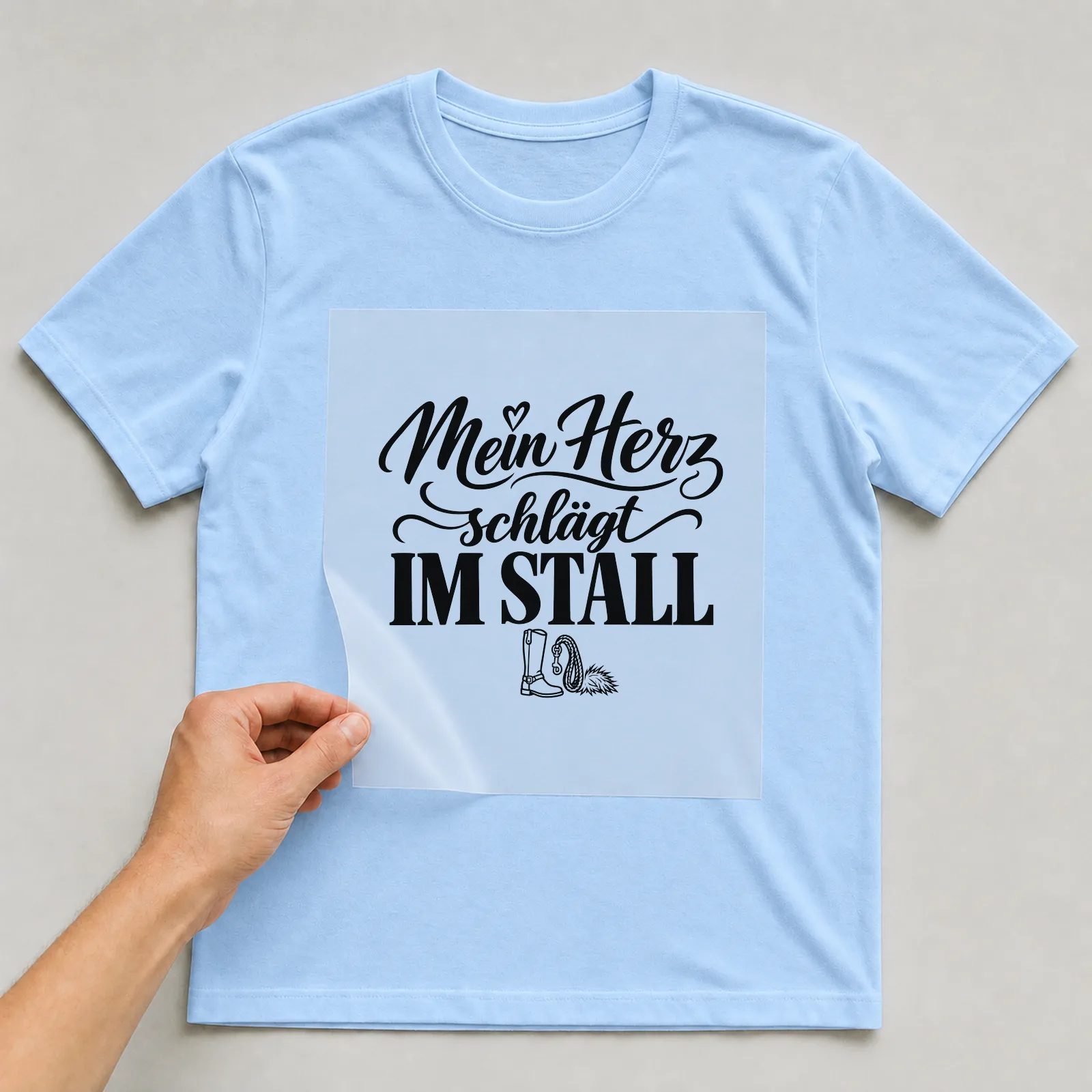 Bügelbild „Mein Herz schlägt im Stall“ auf hellblauem T-Shirt, Folie wird aufgelegt