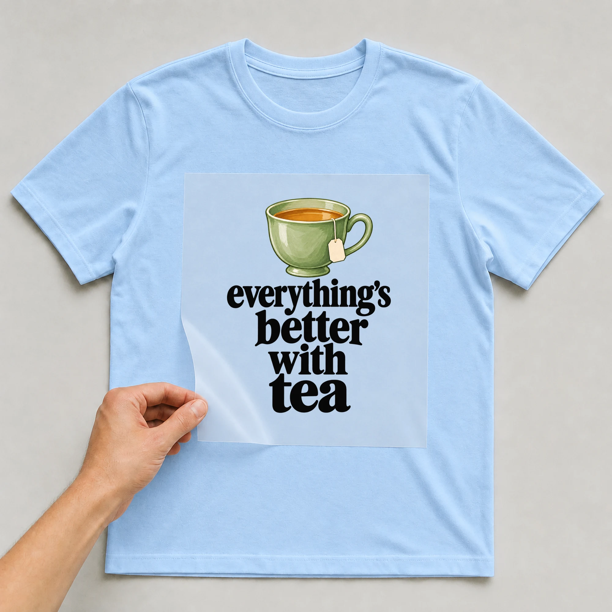 Bügelbild „everything's better with tea“ auf babyblauem T-Shirt, Folie wird aufgelegt