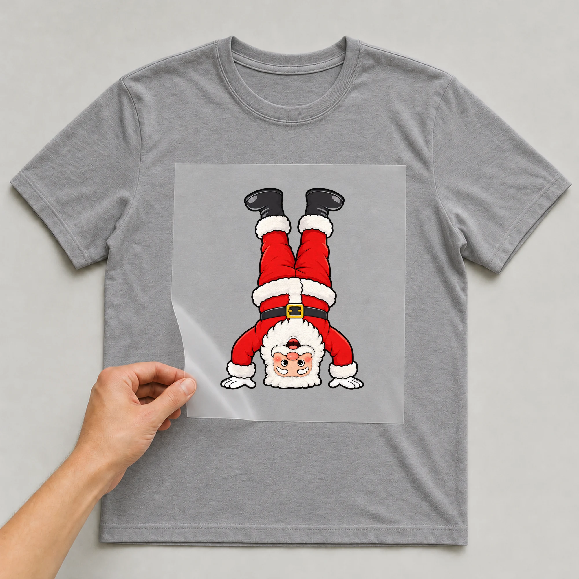 Bügelbild „Weihnachtsmann Kopfstand“ auf grauem T-Shirt, Folie wird aufgelegt
