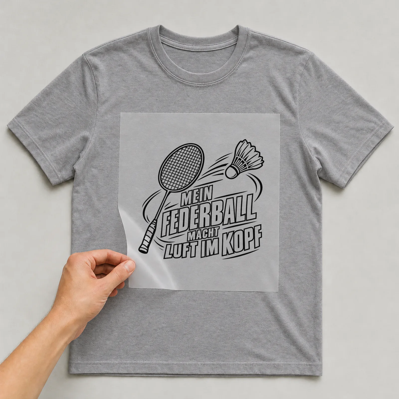 Bügelbild „Mein Federball macht Luft im Kopf“ auf grauem T-Shirt, Folie wird aufgelegt