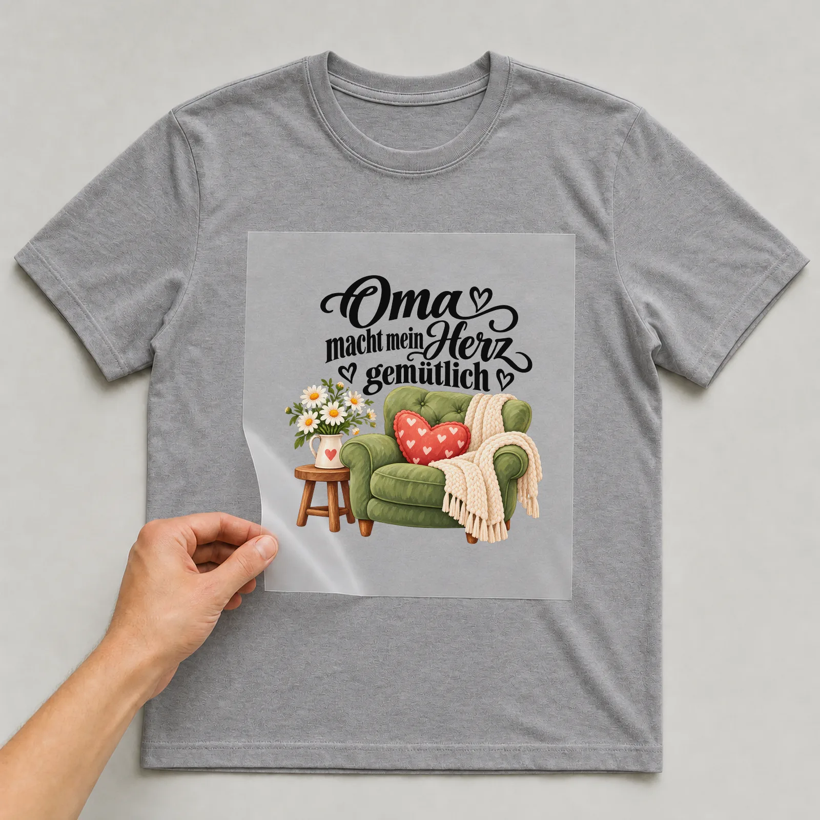 Bügelbild „Oma macht mein Herz gemütlich“ auf grauem T-Shirt, Folie wird aufgelegt