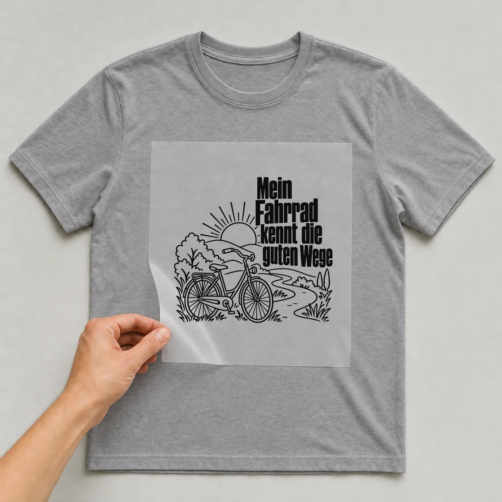 Bügelbild „Mein Fahrrad kennt die guten Wege“ auf grauem T-Shirt, Folie wird aufgelegt