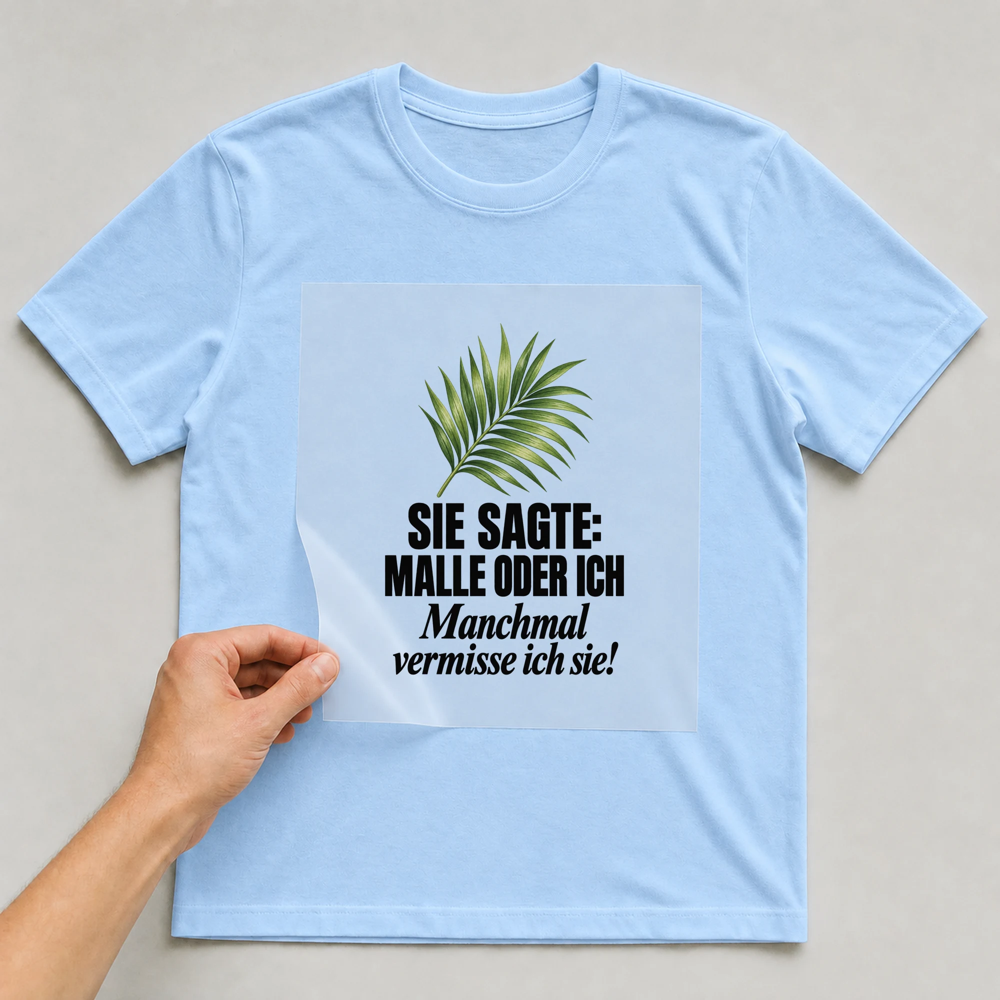 Bügelbild „Sie sagte: Malle oder ich manchmal vermisse ich sie!“ auf babyblauem T-Shirt, Folie wird aufgelegt