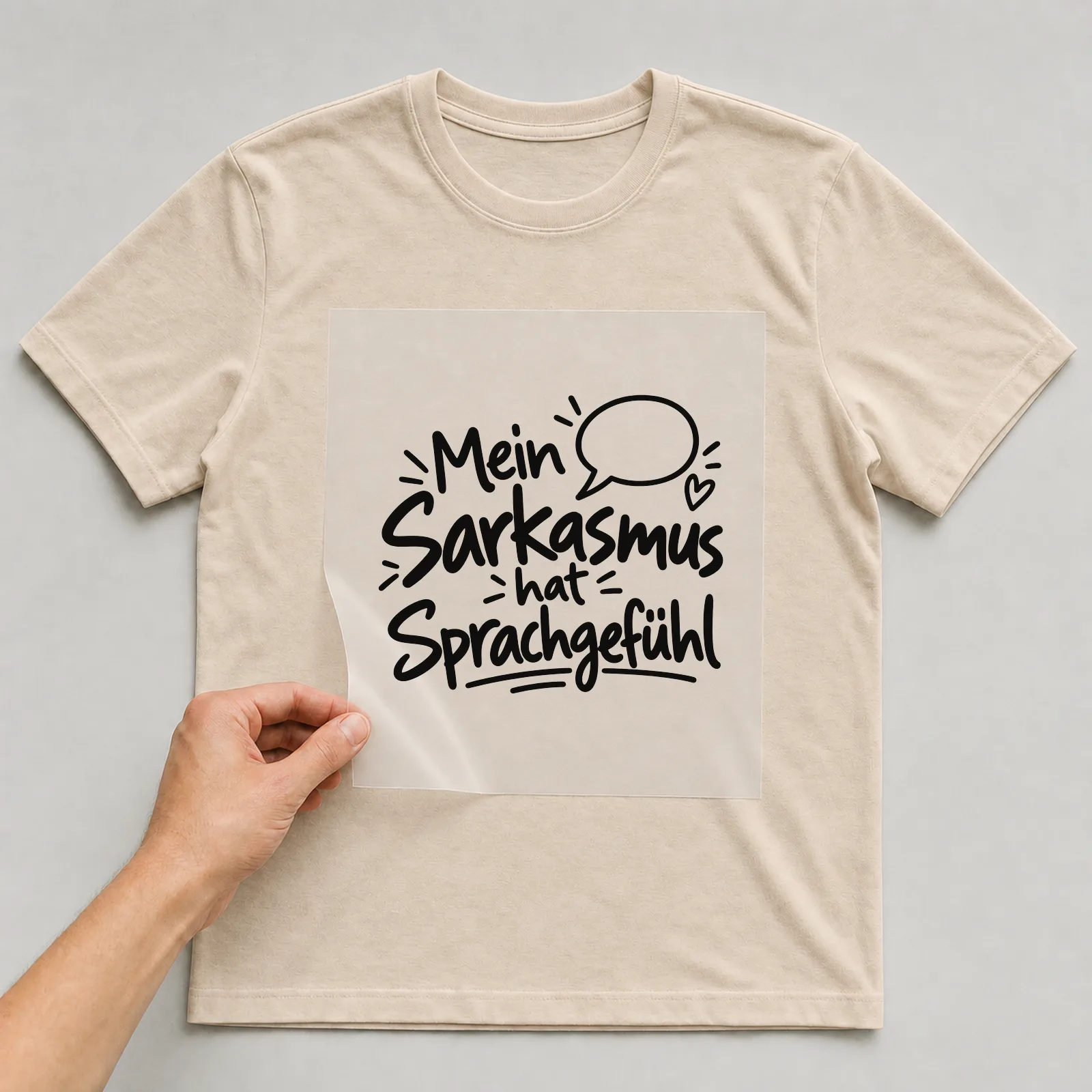 Bügelbild „Mein Sarkasmus hat Sprachgefühl“ auf beigem T-Shirt, Folie wird aufgelegt