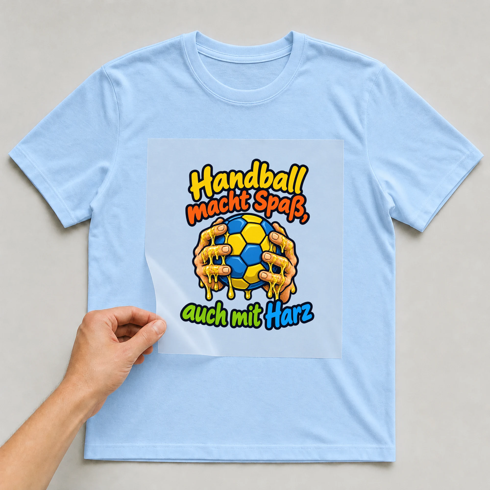 Bügelbild „Handball macht Spaß, auch mit Harz“ auf babyblauem T-Shirt, Folie wird aufgelegt