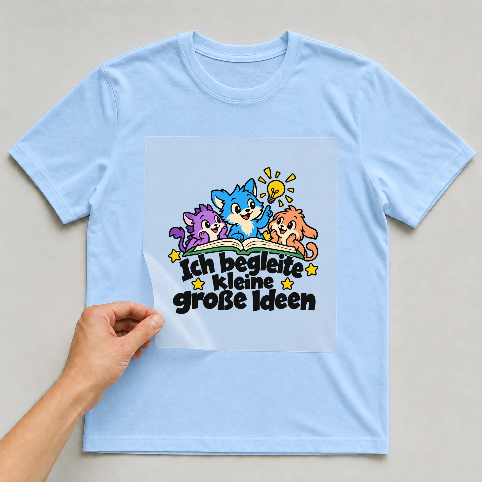 Bügelbild „Ich begleite kleine große Ideen“ auf babyblauem T-Shirt, Folie wird aufgelegt