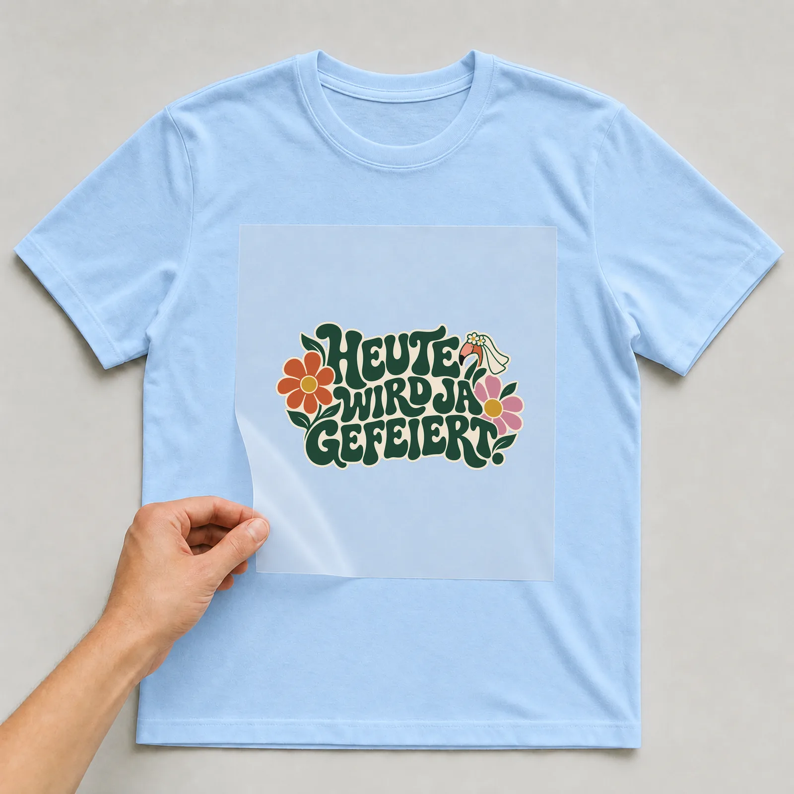 Bügelbild „Heute wird ja gefeiert“ auf hellblauem T-Shirt, Folie wird aufgelegt