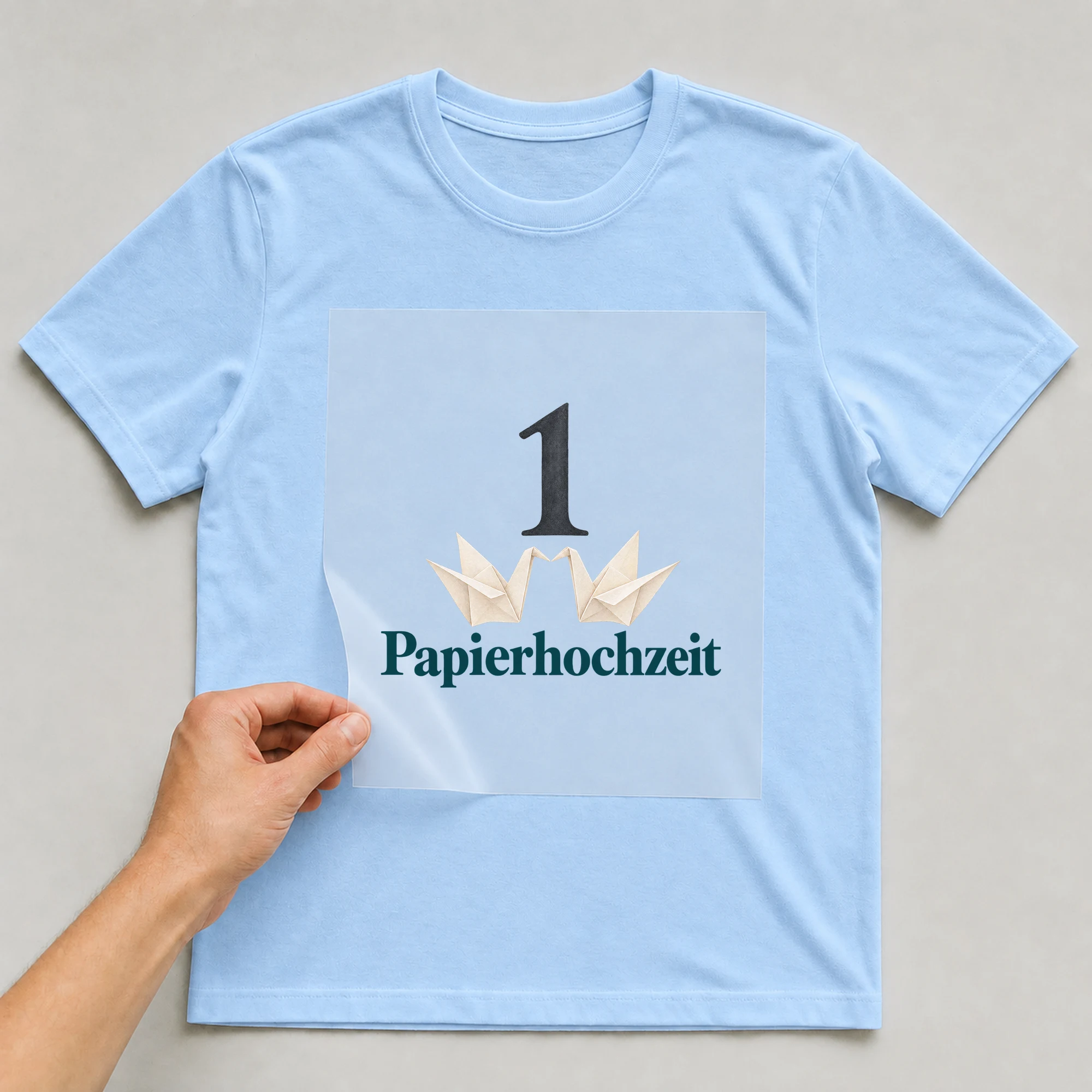 Bügelbild „1 Papierhochzeit“ auf babyblauem T-Shirt, Folie wird aufgelegt