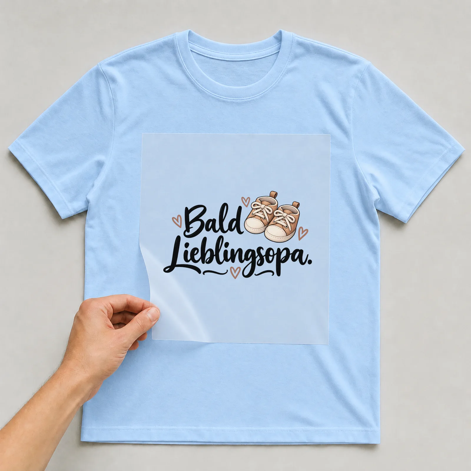 Bügelbild „Bald Lieblingsopa“ auf hellblauem T-Shirt, Folie wird aufgelegt