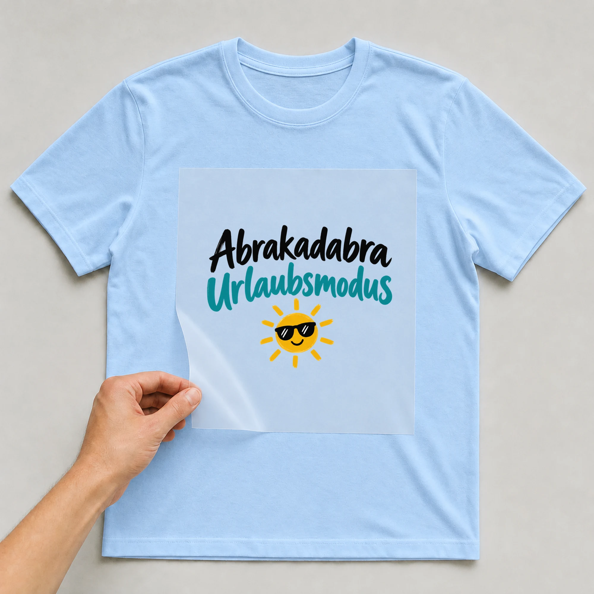 Bügelbild „Abrakadabra, Urlaubsmodus“ auf babyblauem T-Shirt, Folie wird aufgelegt