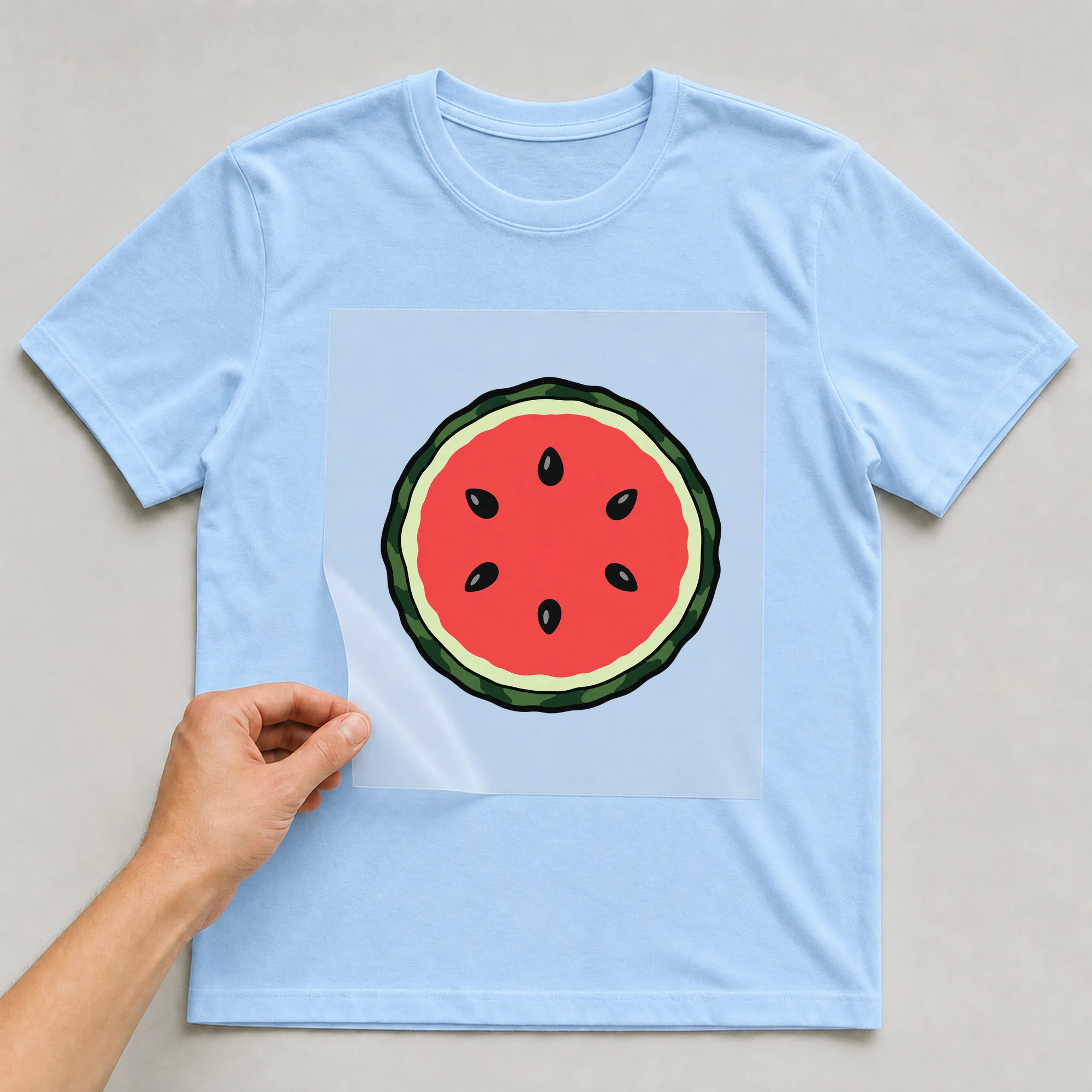 Bügelbild „Wassermelone Rund“ auf babyblauem T-Shirt, Folie wird aufgelegt