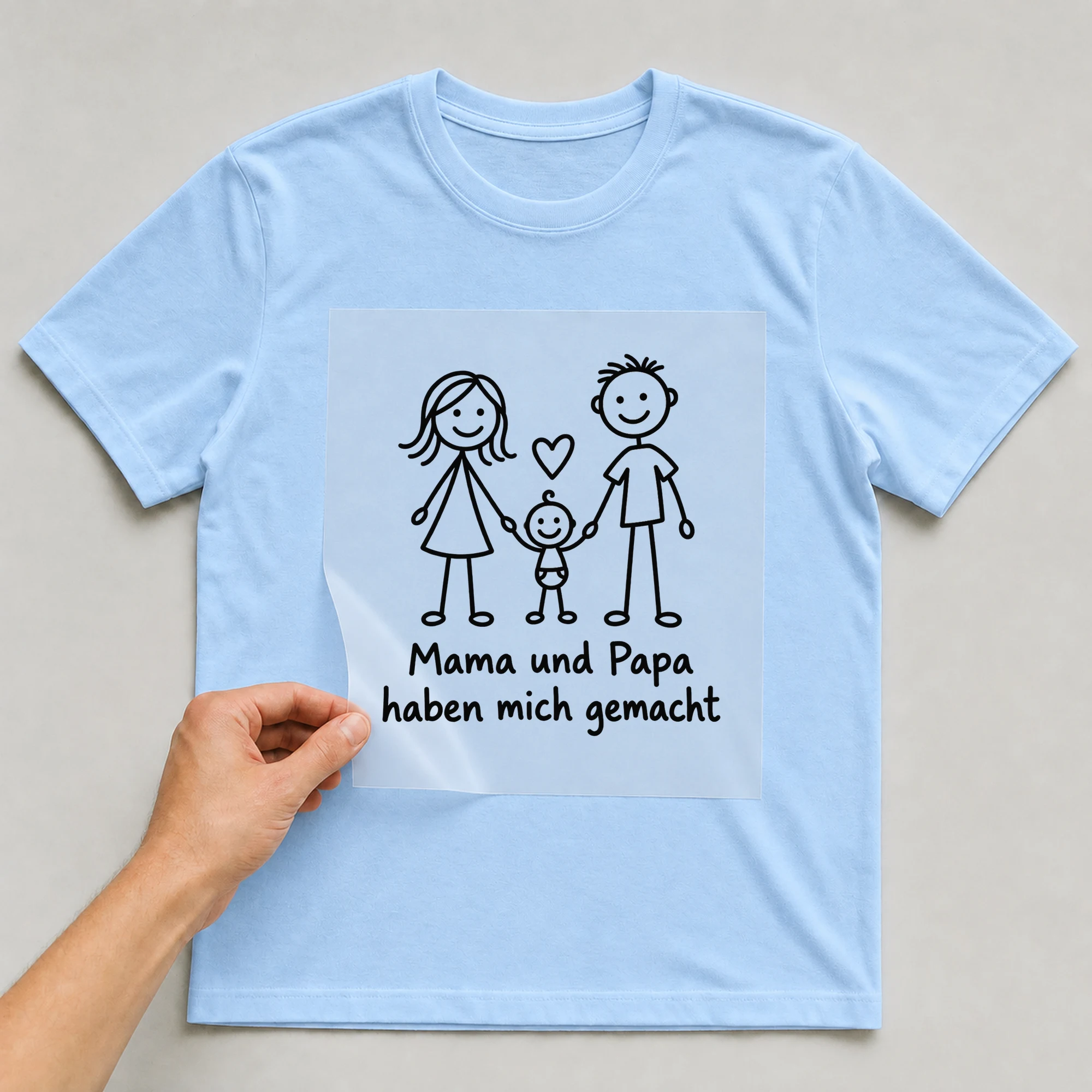 Bügelbild „Mama und Papa haben mich gemacht“ auf babyblauem T-Shirt, Folie wird aufgelegt