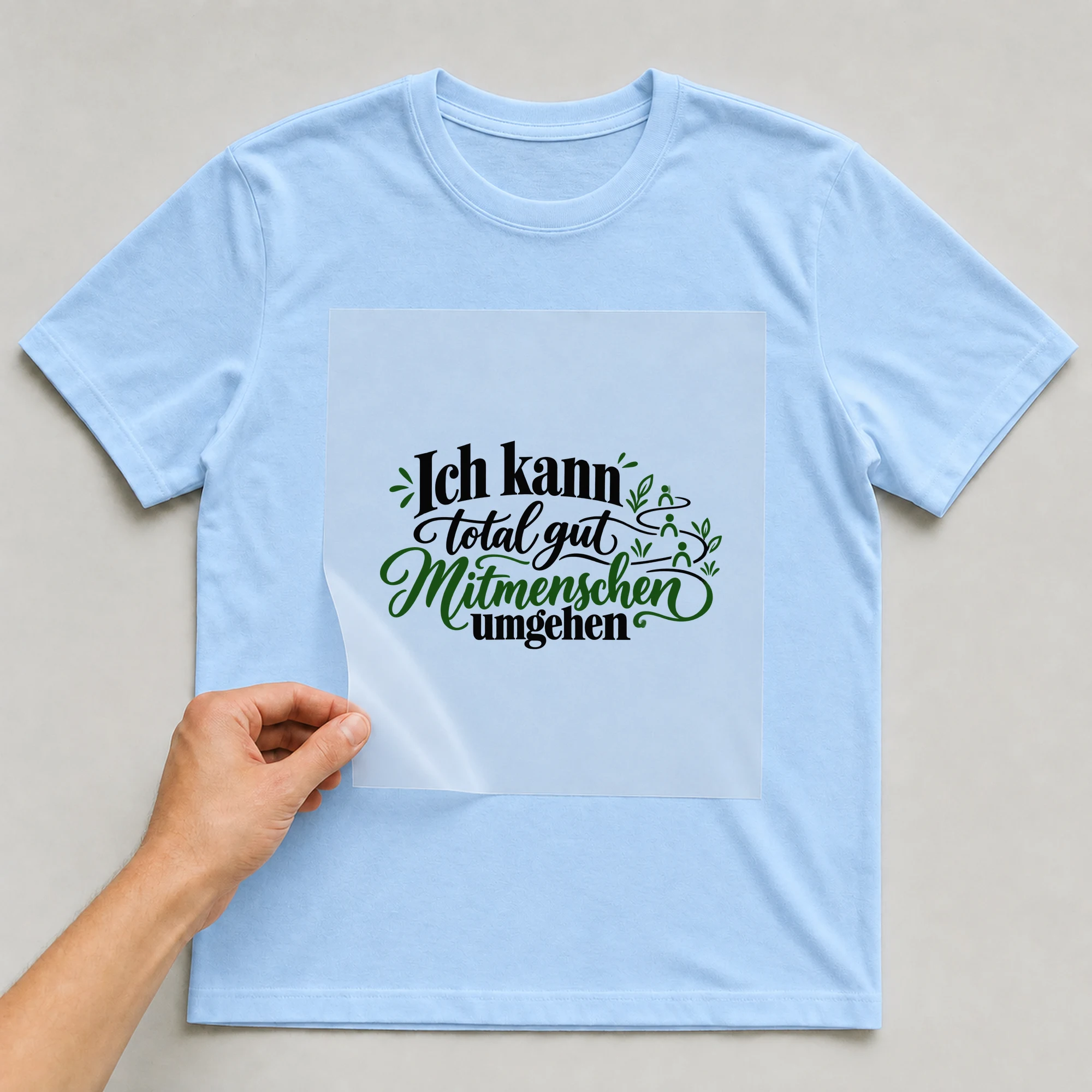 Bügelbild „Ich kann total gut Mitmenschen umgehen“ auf babyblauem T-Shirt, Folie wird aufgelegt