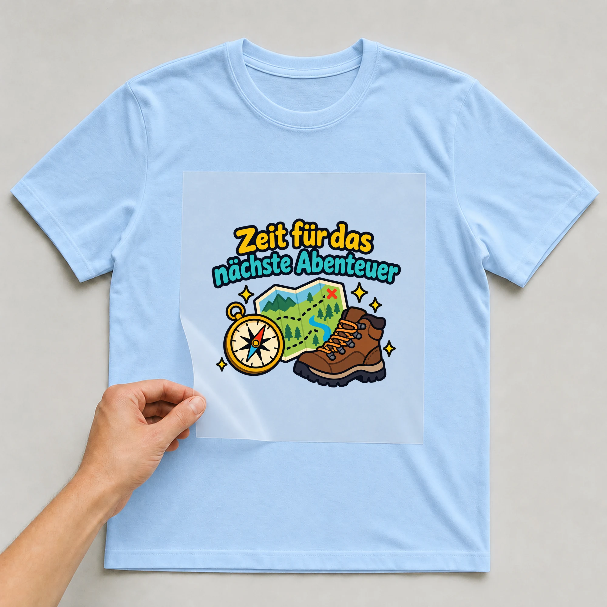 Bügelbild „Zeit für das nächste Abenteuer“ auf babyblauem T-Shirt, Folie wird aufgelegt