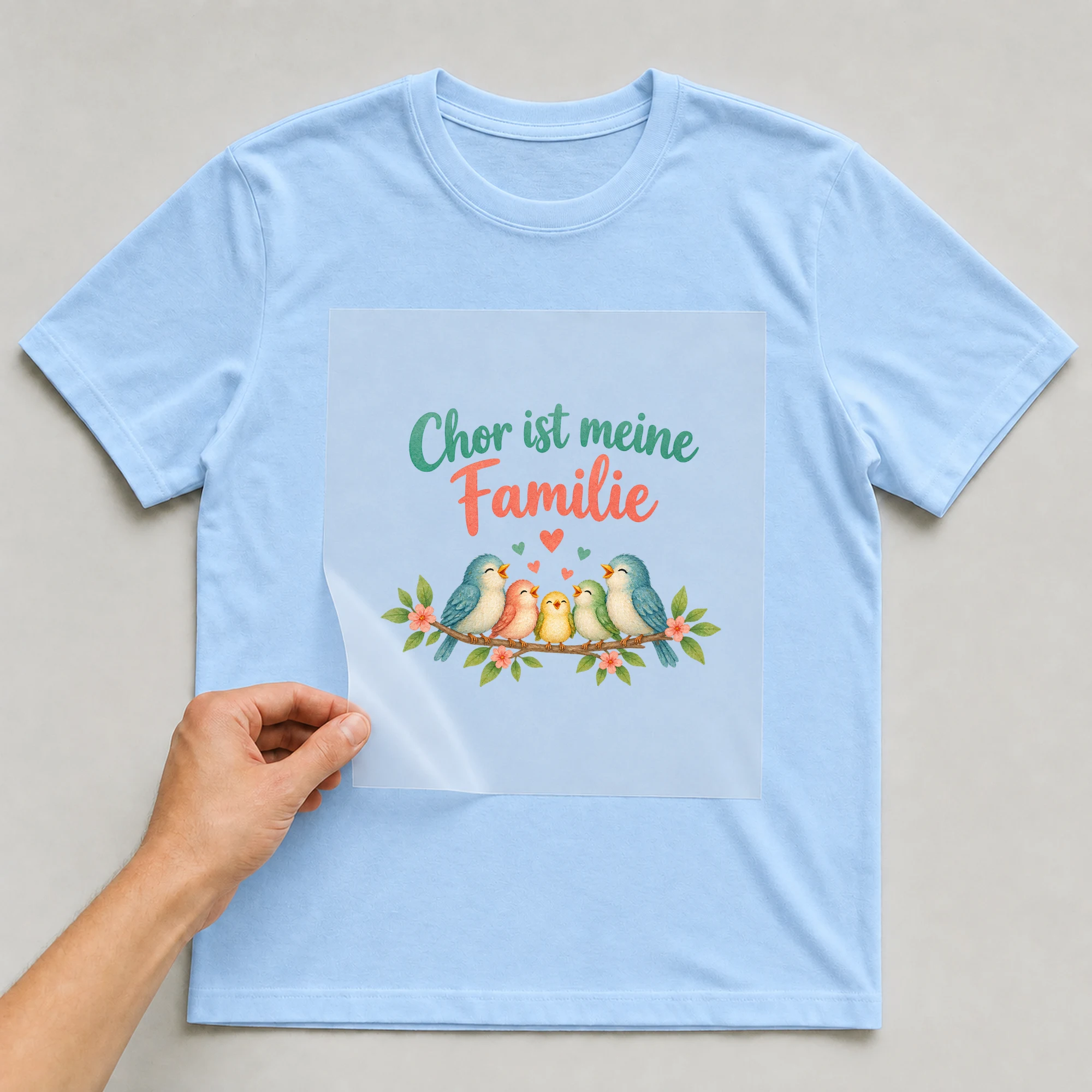 Bügelbild „Chor ist meine Familie“ auf babyblauem T-Shirt, Folie wird aufgelegt