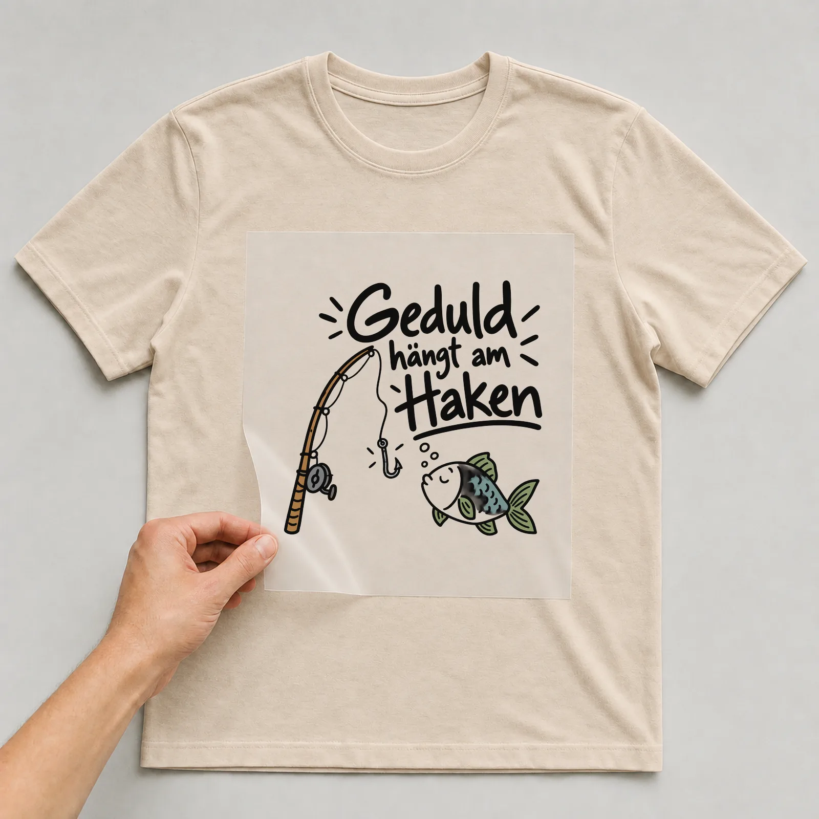 Bügelbild „Geduld hängt am Haken“ auf beigem T-Shirt, Folie wird aufgelegt