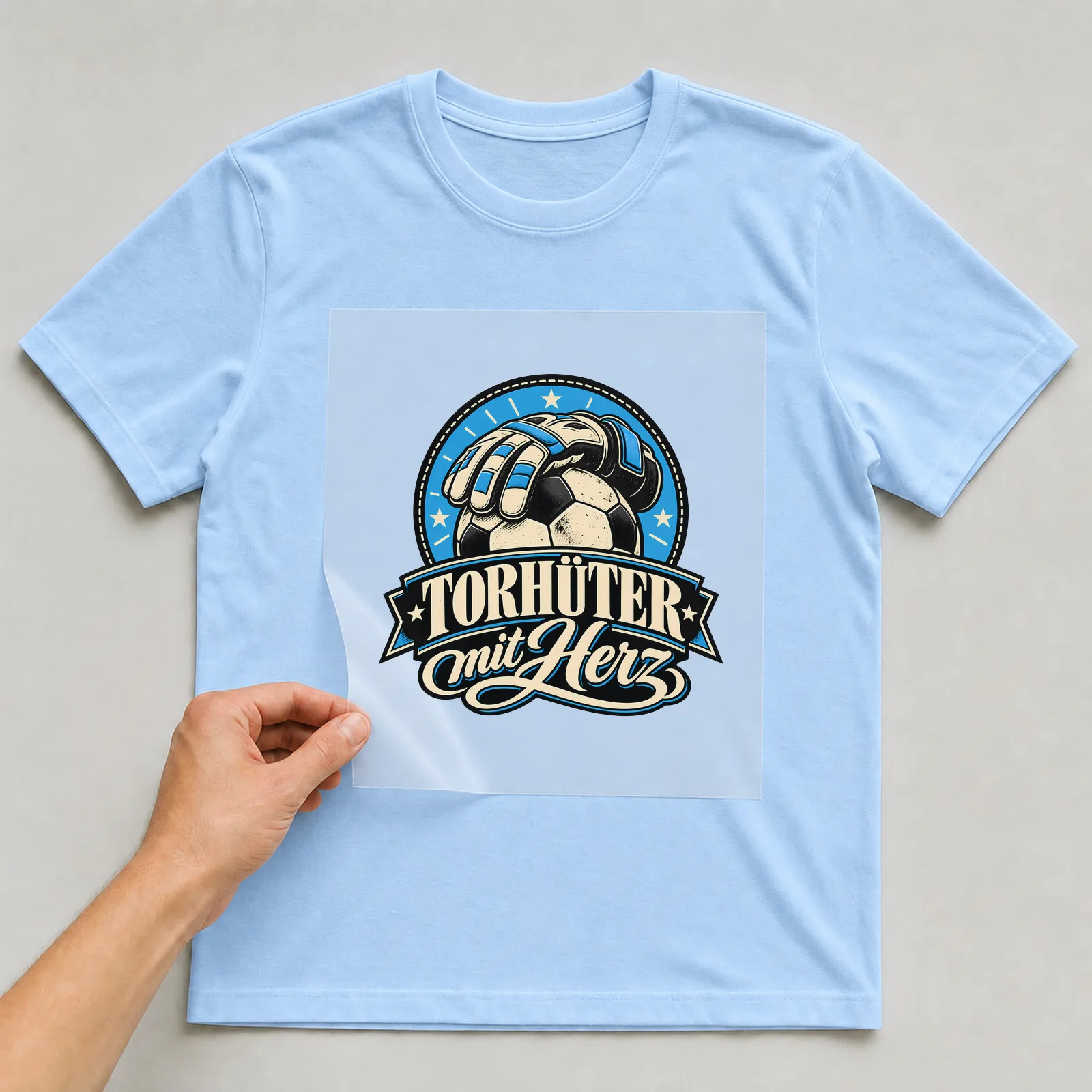 Bügelbild „Torhüter mit Herz“ auf hellblauem T-Shirt, Folie wird aufgelegt