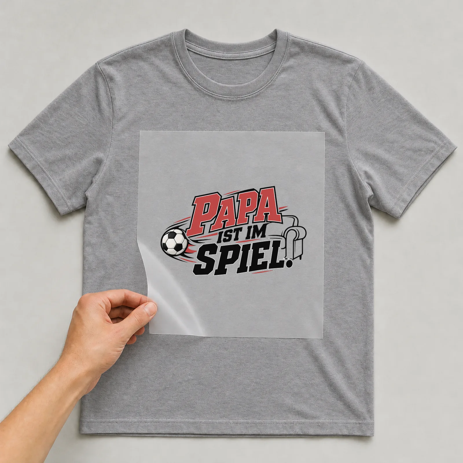 Bügelbild „Papa ist im Spiel“ auf grauem T-Shirt, Folie wird aufgelegt