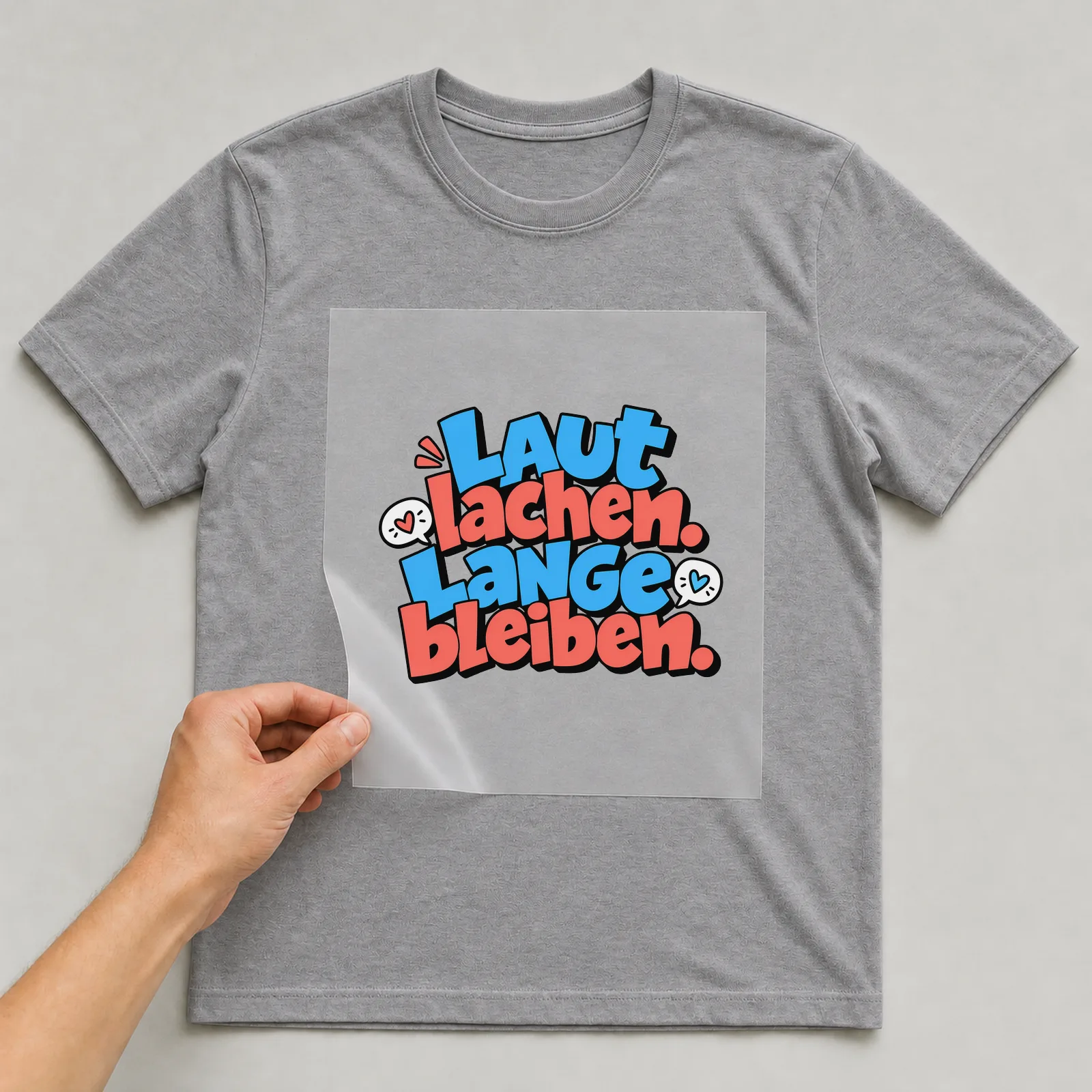 Bügelbild „Laut lachen. Lange bleiben.“ auf grauem T-Shirt, Folie wird aufgelegt