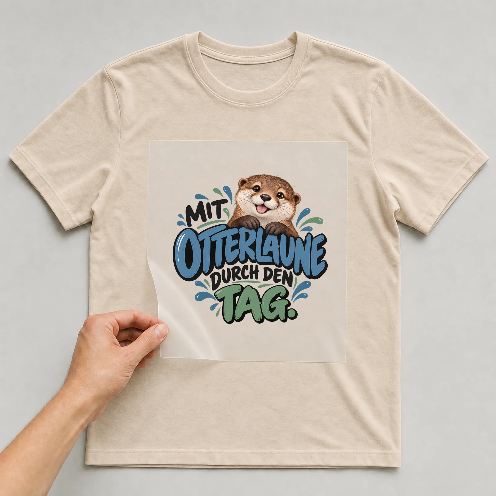 Bügelbild „Mit Otterlaune durch den Tag“ auf beigem T-Shirt, Folie wird aufgelegt