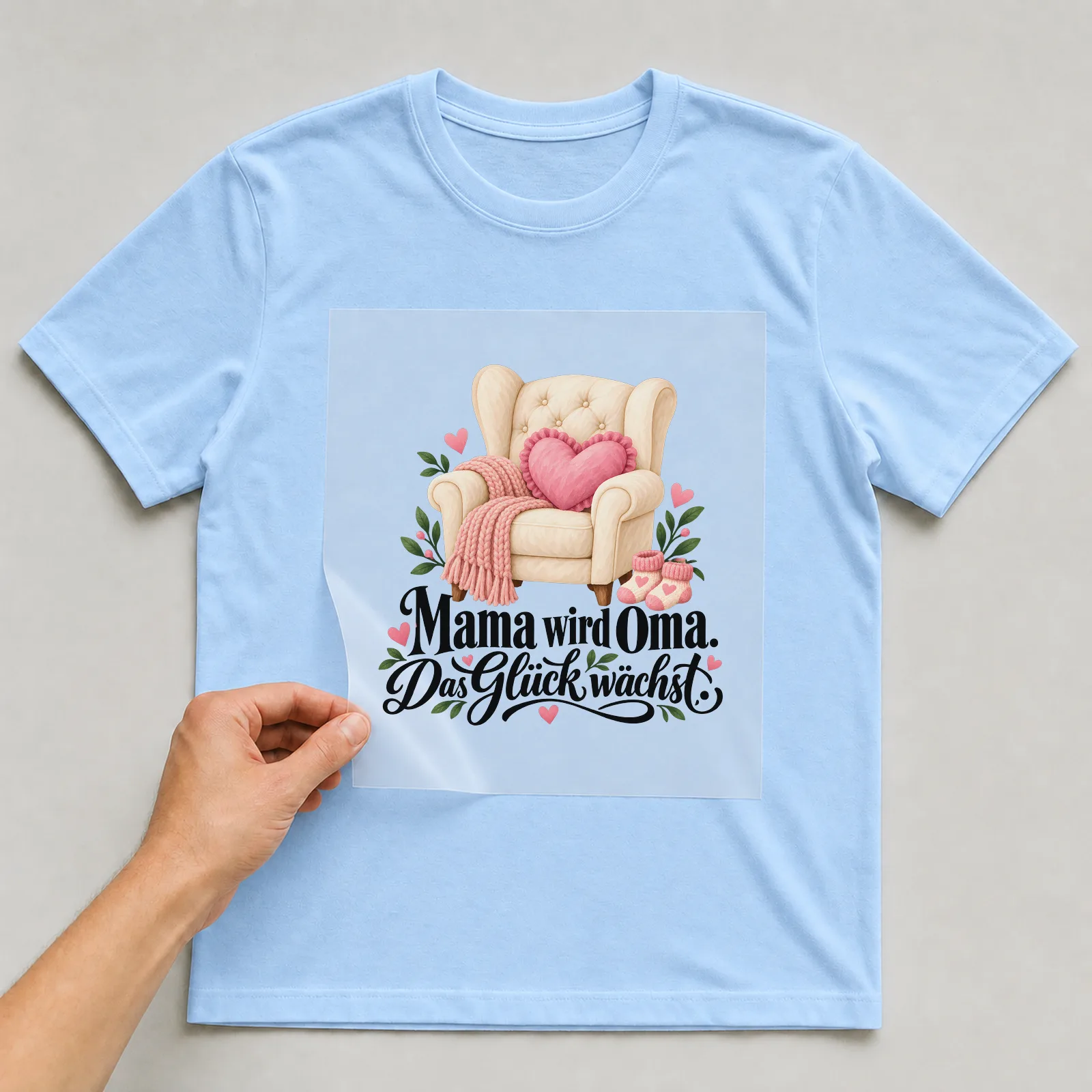 Bügelbild „Mama wird Oma. Das Glück wächst.“ auf hellblauem T-Shirt, Folie wird aufgelegt