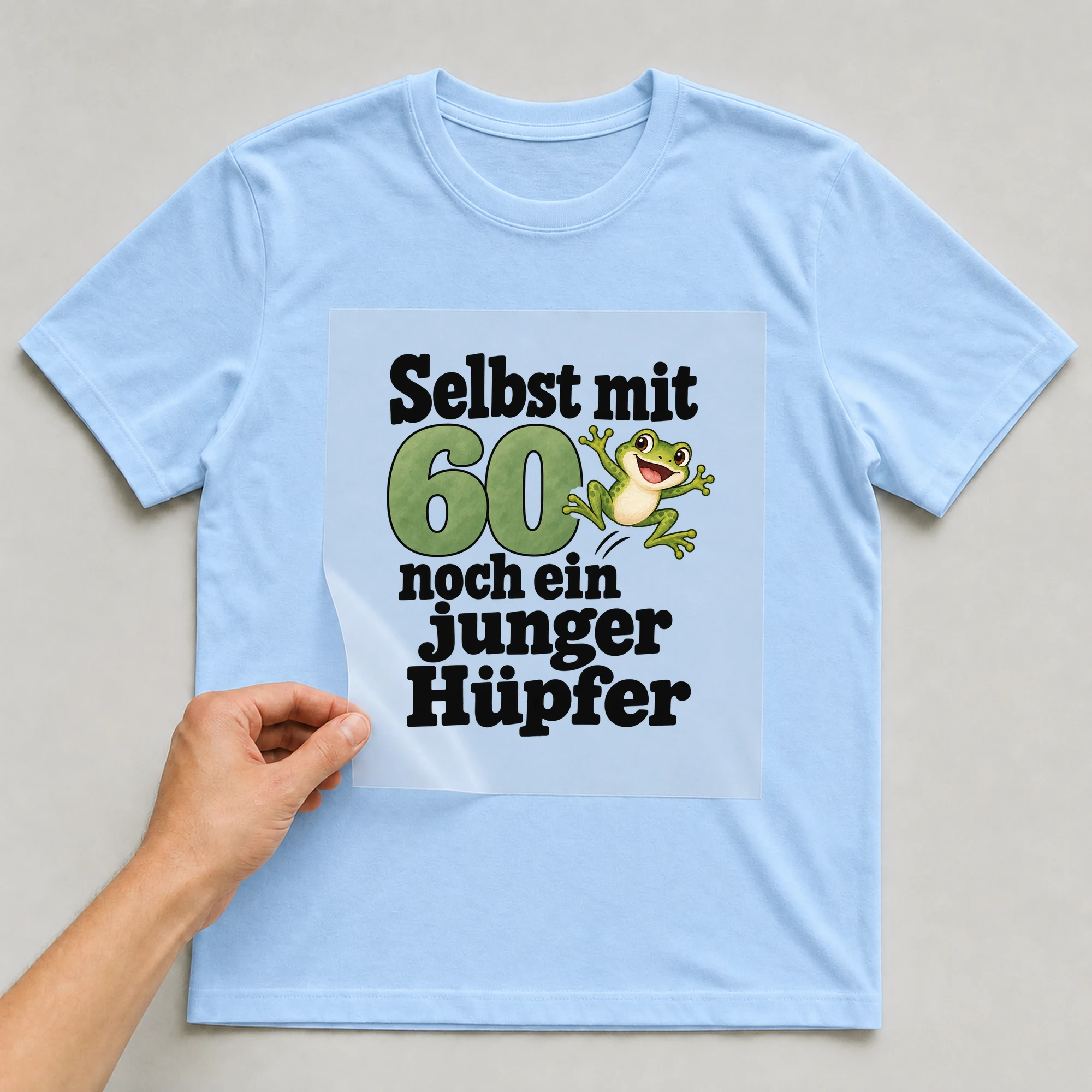 Bügelbild „Selbst mit 60 noch ein junger Hüpfer“ auf babyblauem T-Shirt, Folie wird aufgelegt