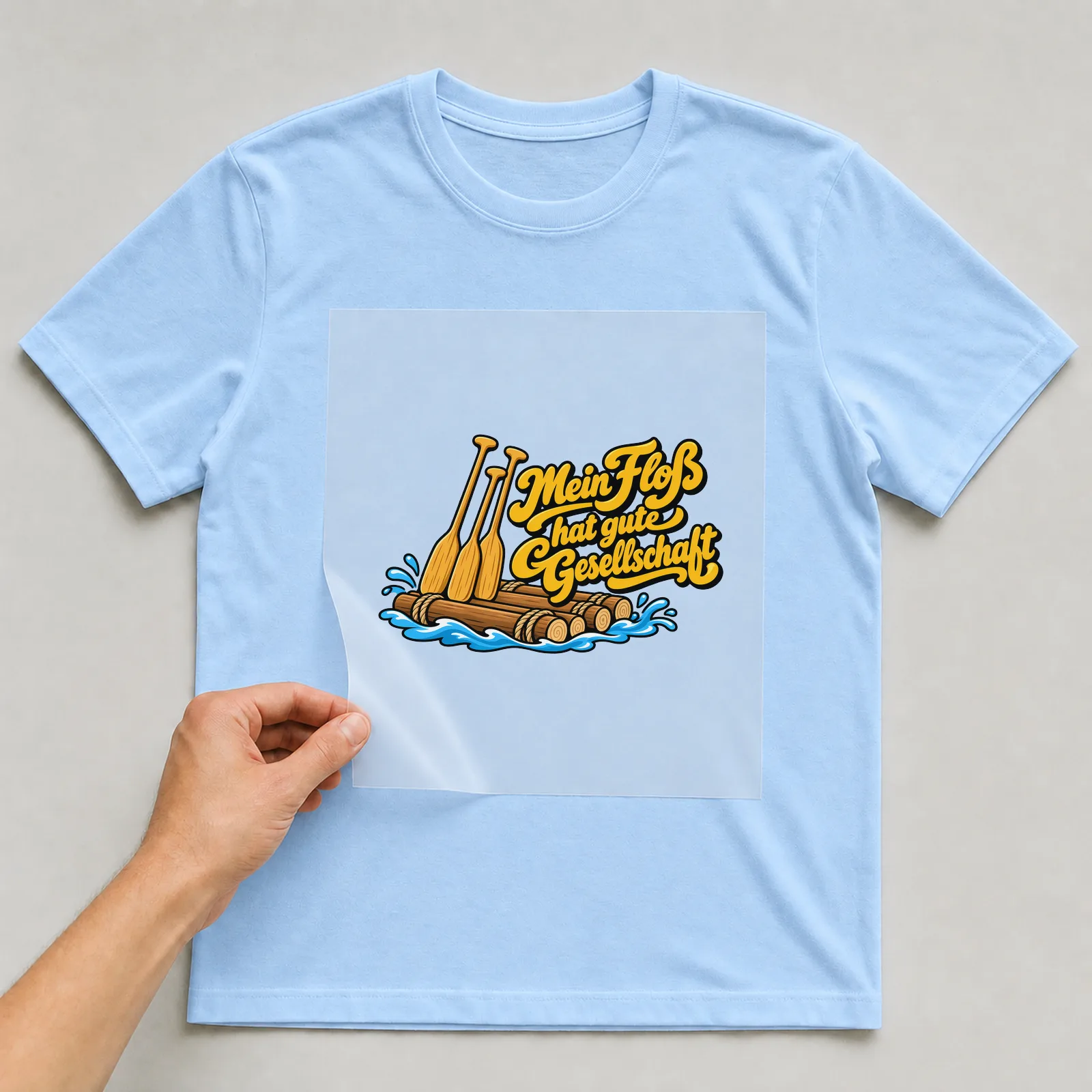 Bügelbild „Mein Floß hat gute Gesellschaft“ auf hellblauem T-Shirt, Folie wird aufgelegt