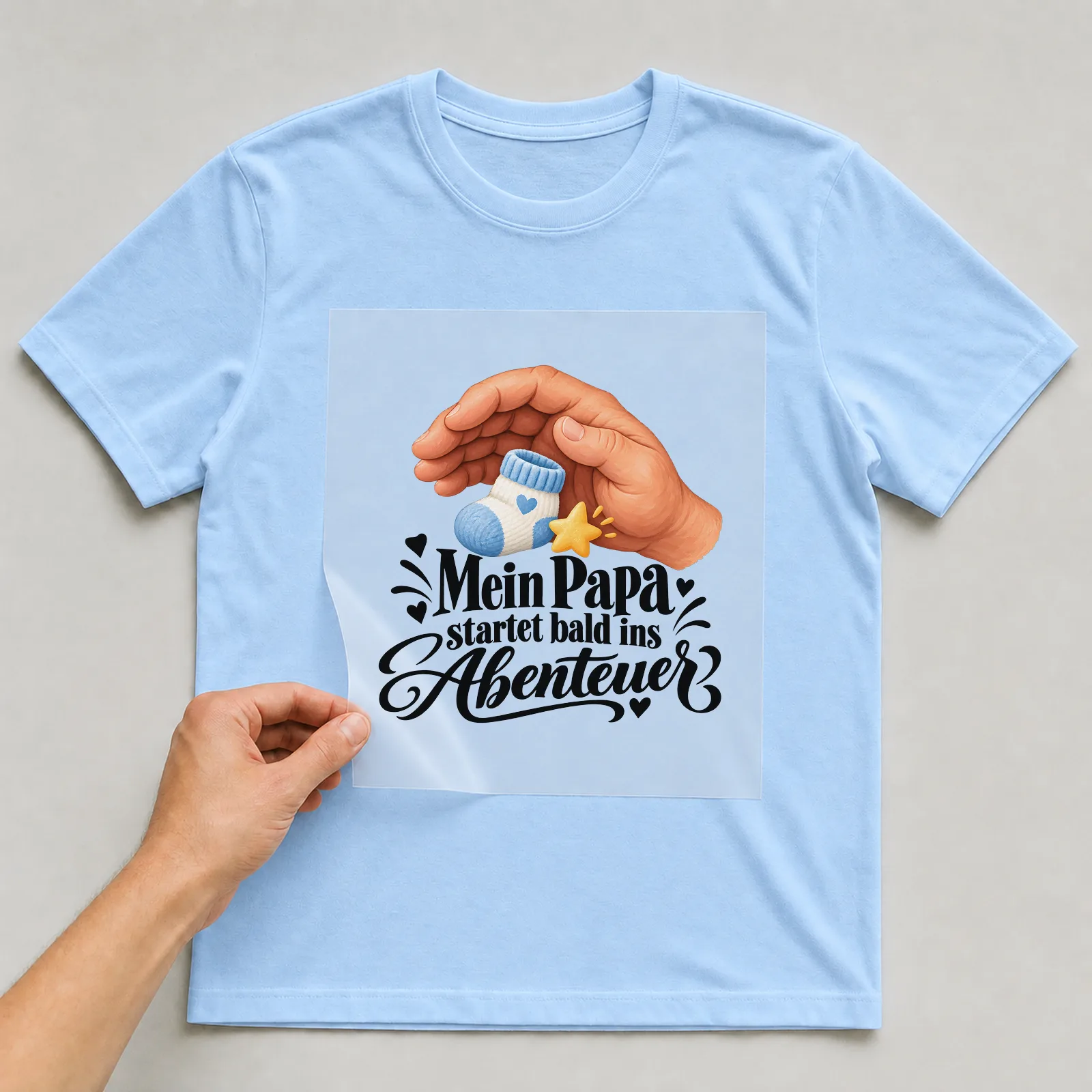 Bügelbild „Mein Papa startet bald ins Abenteuer“ auf hellblauem T-Shirt, Folie wird aufgelegt