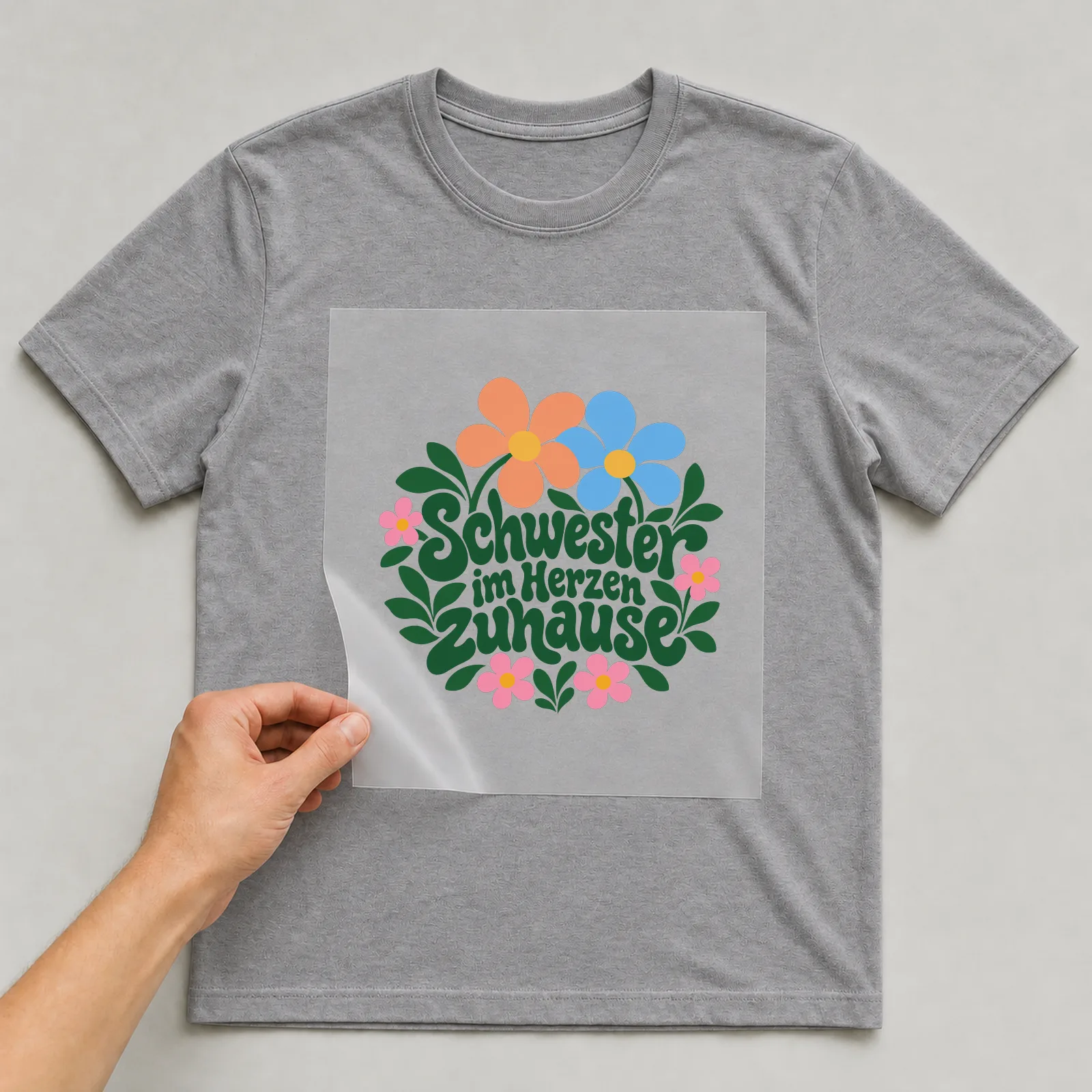 Bügelbild „Schwester im Herzen zuhause“ auf grauem T-Shirt, Folie wird aufgelegt