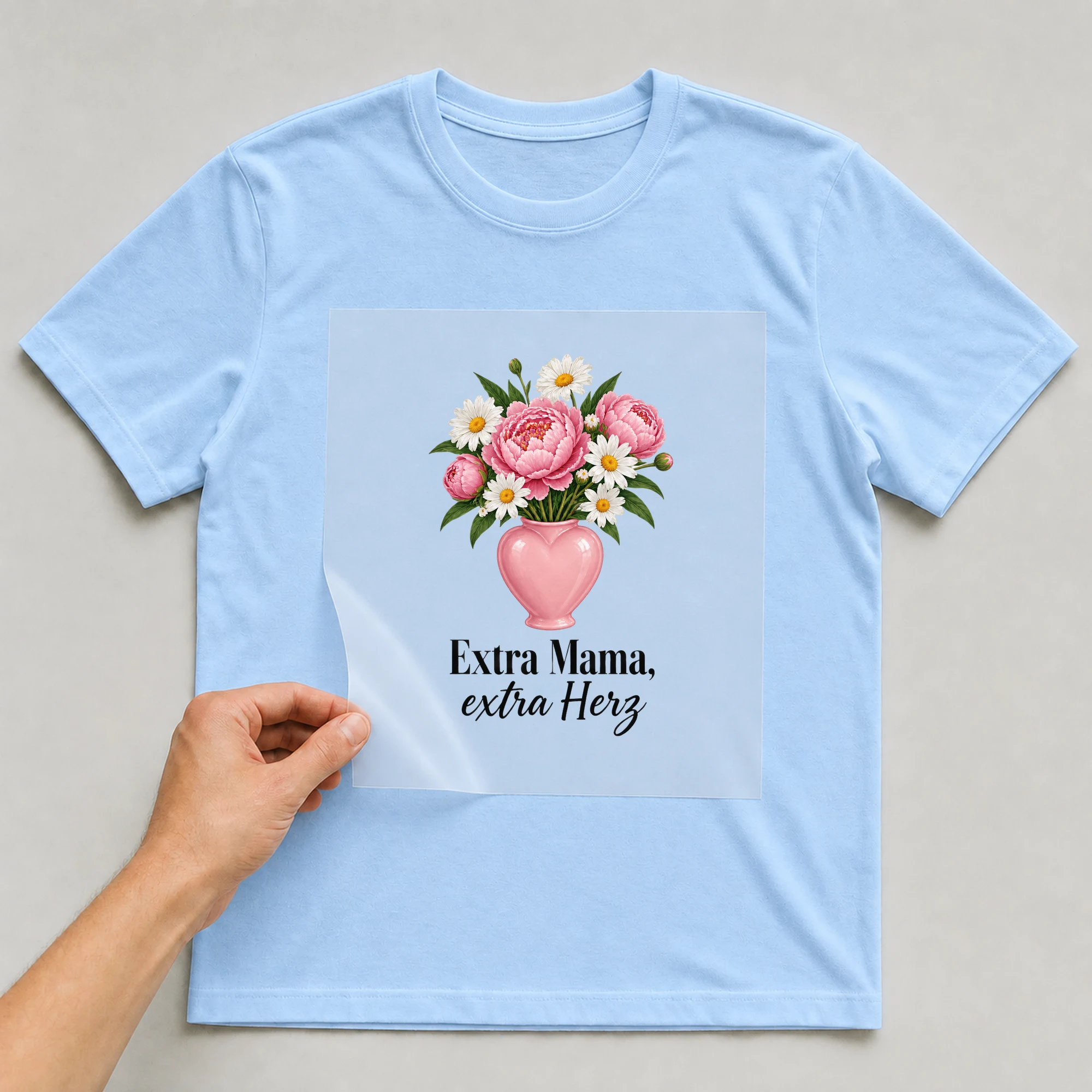 Bügelbild „Extra Mama, extra Herz“ auf hellblauem T-Shirt, Folie wird aufgelegt