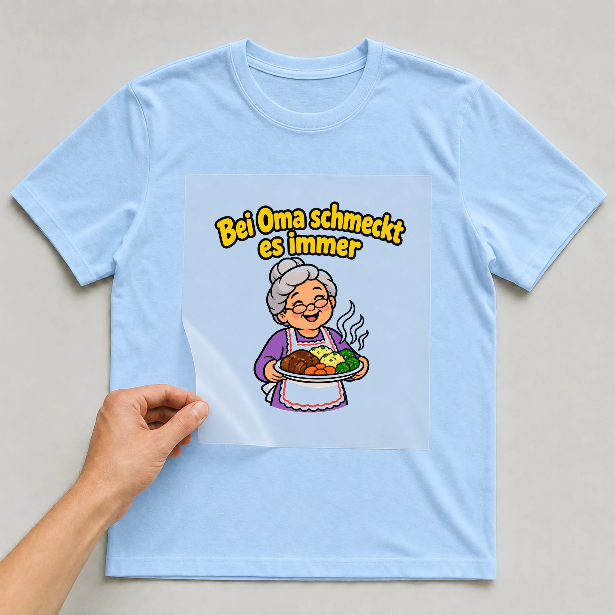 Bügelbild „Bei Oma schmeckt es immer“ auf babyblauem T-Shirt, Folie wird aufgelegt