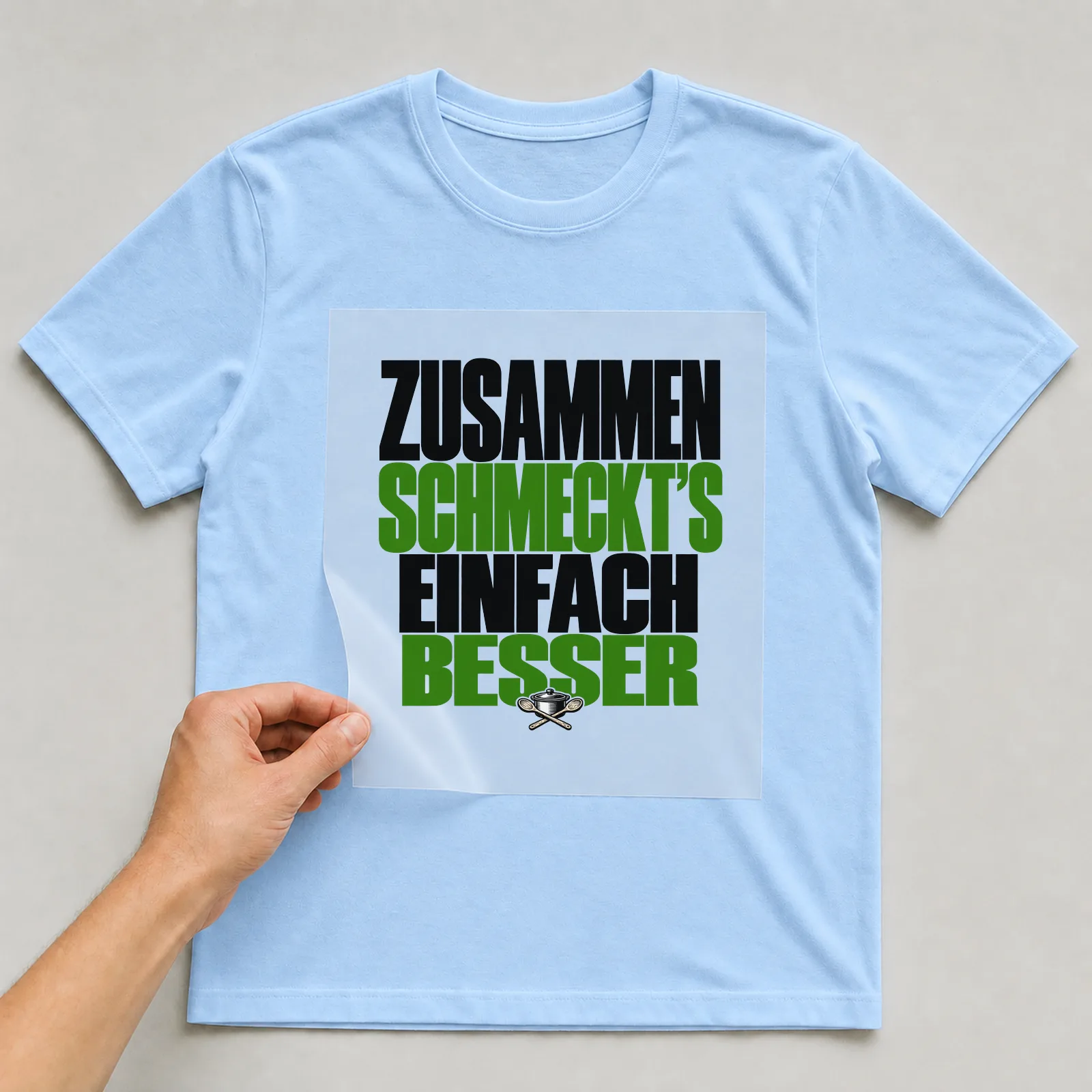 Bügelbild „Zusammen schmeckt’s einfach besser“ auf hellblauem T-Shirt, Folie wird aufgelegt