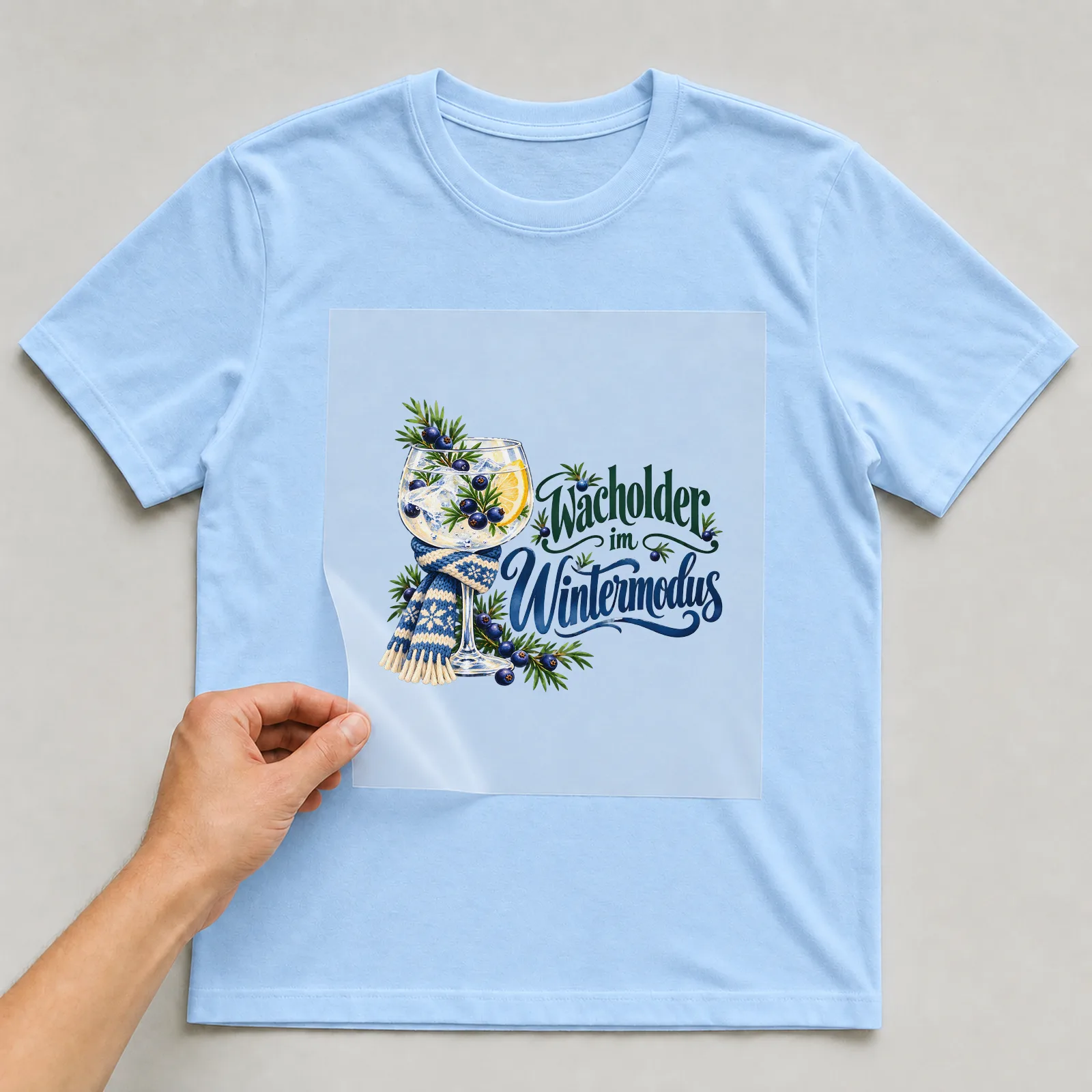 Bügelbild „Wacholder im Wintermodus“ auf hellblauem T-Shirt, Folie wird aufgelegt