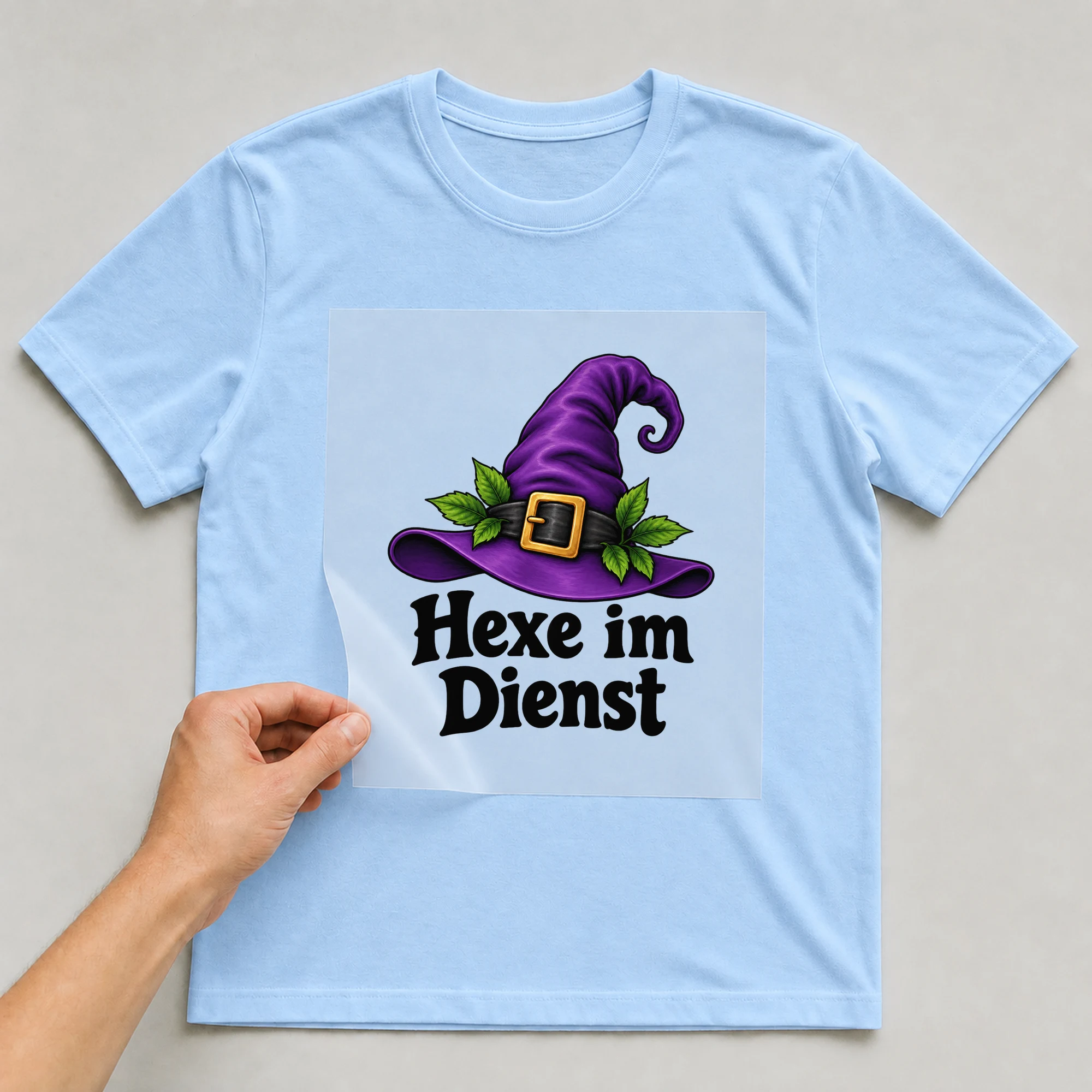Bügelbild „Hexe im Dienst“ auf babyblauem T-Shirt, Folie wird aufgelegt