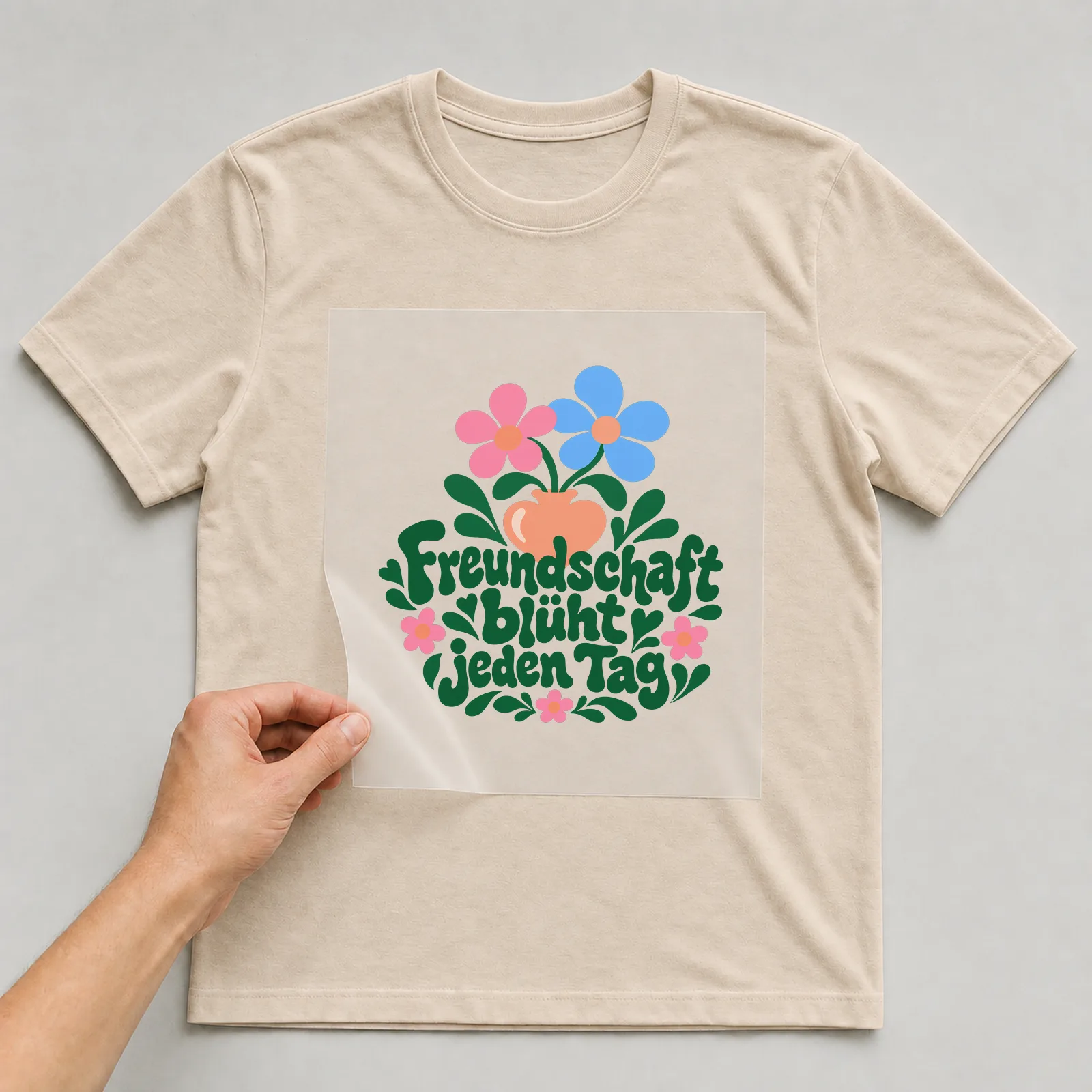 Bügelbild „Freundschaft blüht jeden Tag“ auf beigem T-Shirt, Folie wird aufgelegt