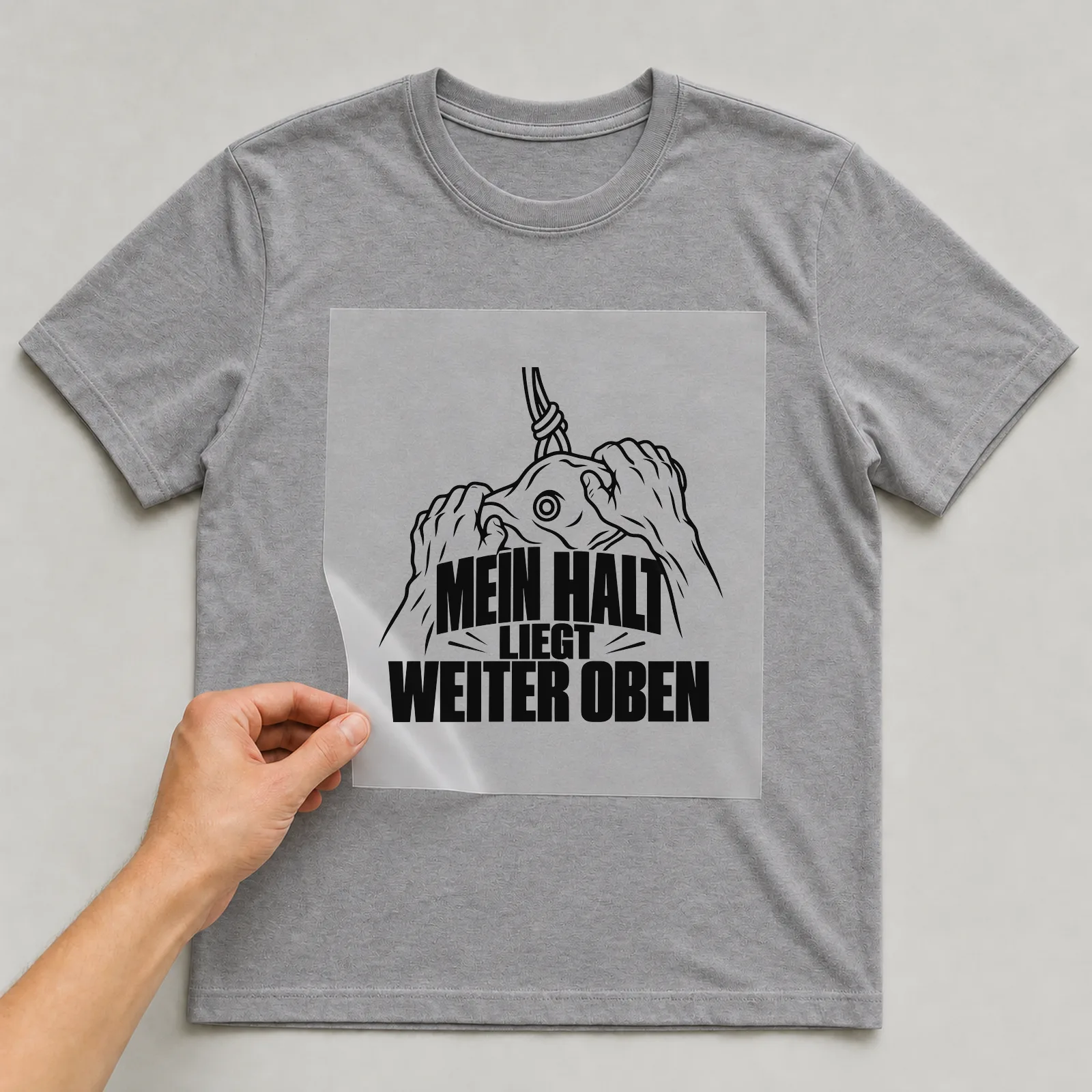Bügelbild „Mein halt liegt weiter oben“ auf grauem T-Shirt, Folie wird aufgelegt