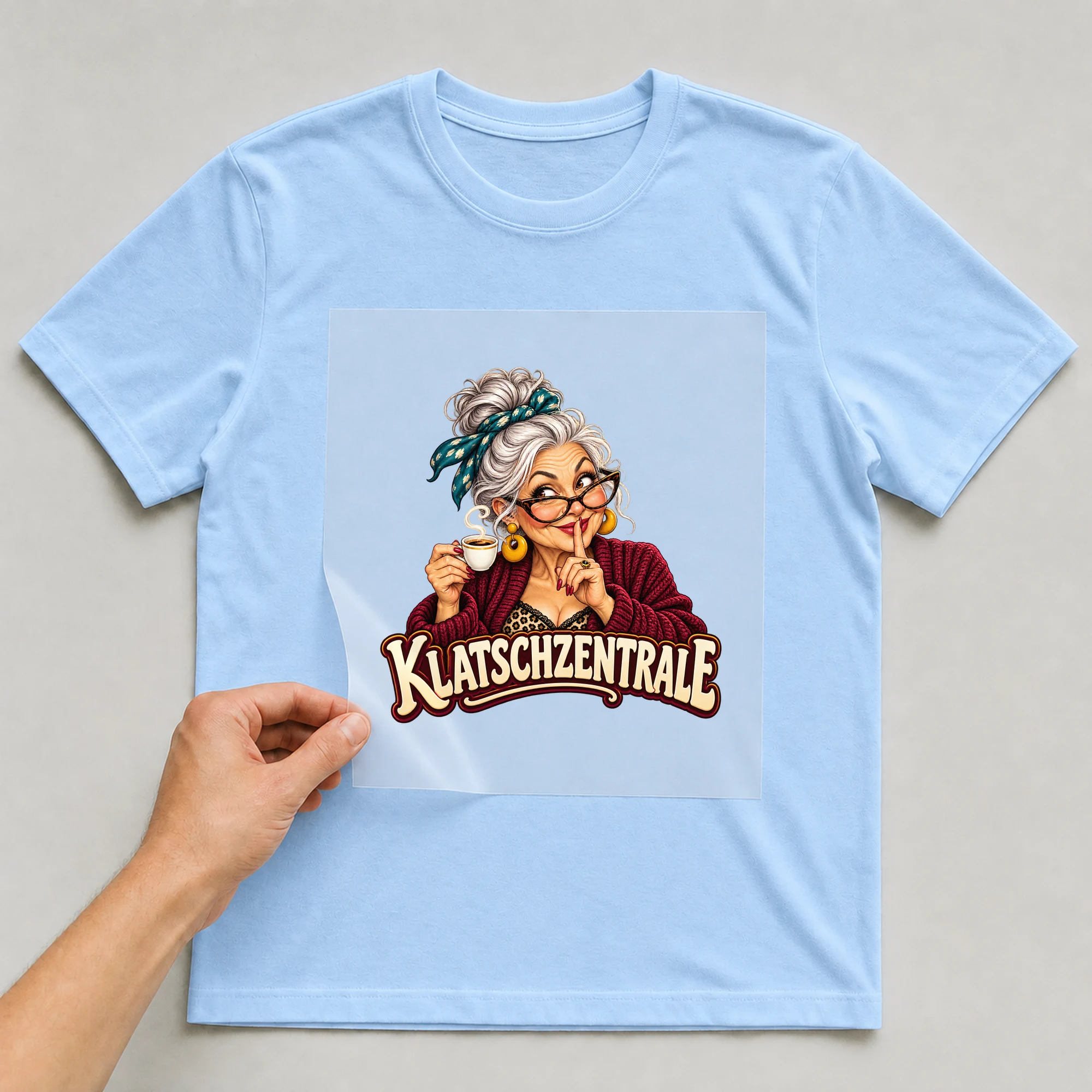 Bügelbild „Klatschzentrale“ auf babyblauem T-Shirt, Folie wird aufgelegt