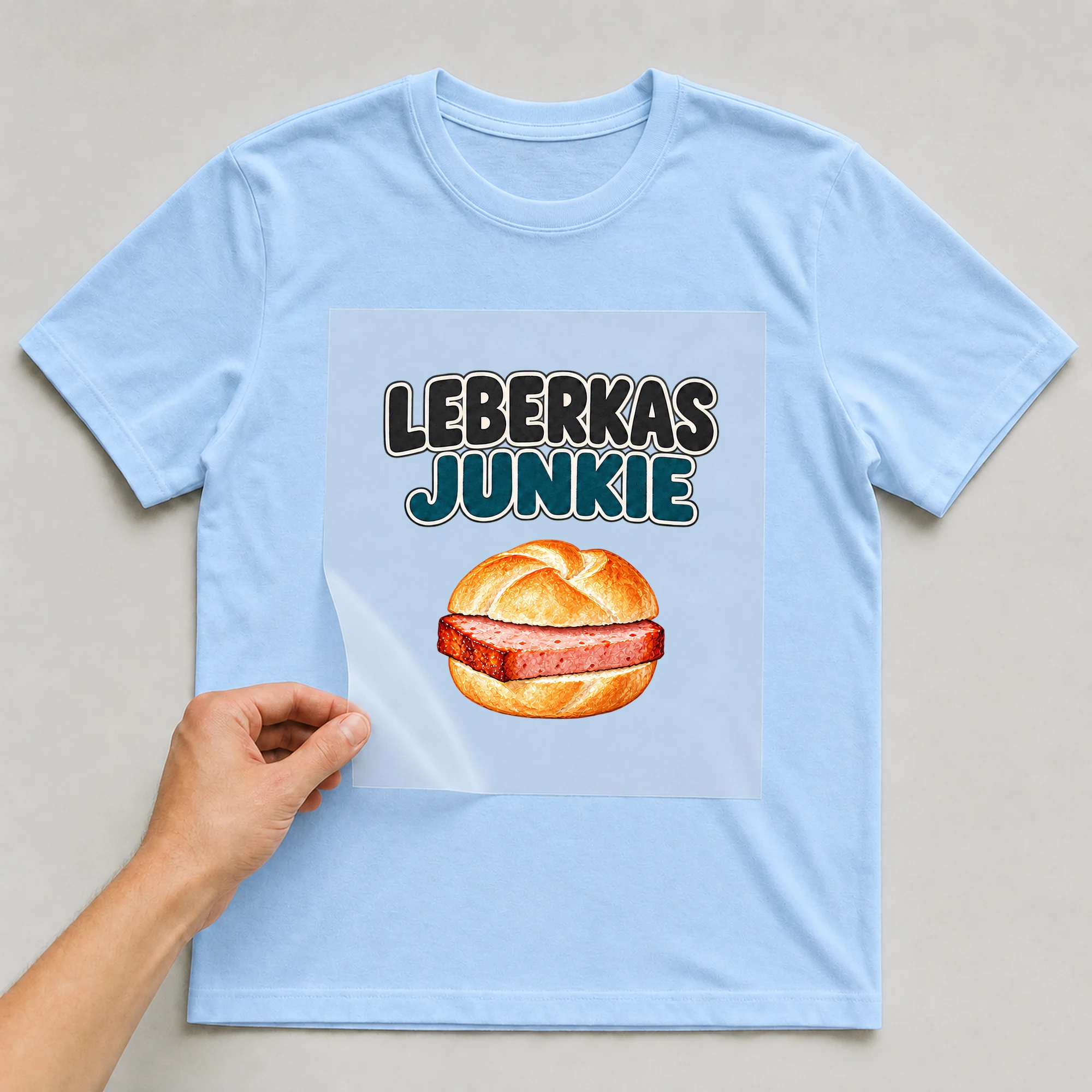Bügelbild „LEBERKAS JUNKIE“ auf babyblauem T-Shirt, Folie wird aufgelegt