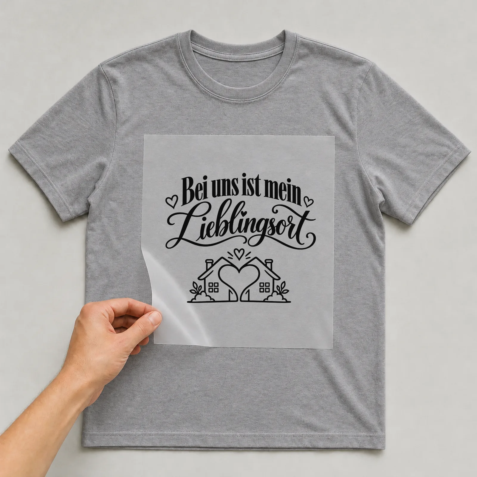 Bügelbild „Bei uns ist mein Lieblingsort“ auf grauem T-Shirt, Folie wird aufgelegt