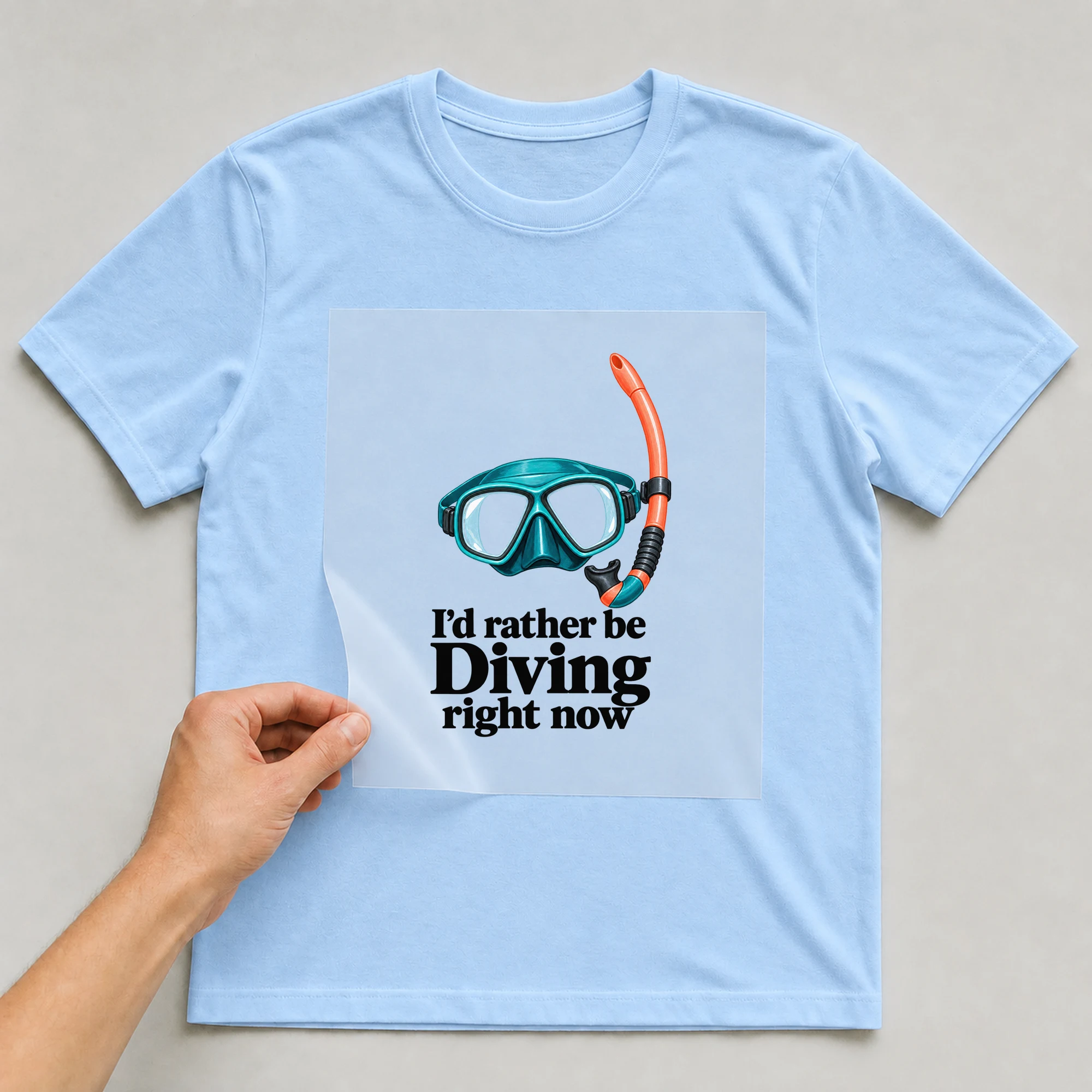 Bügelbild „I'd rather be Diving right now“ auf babyblauem T-Shirt, Folie wird aufgelegt