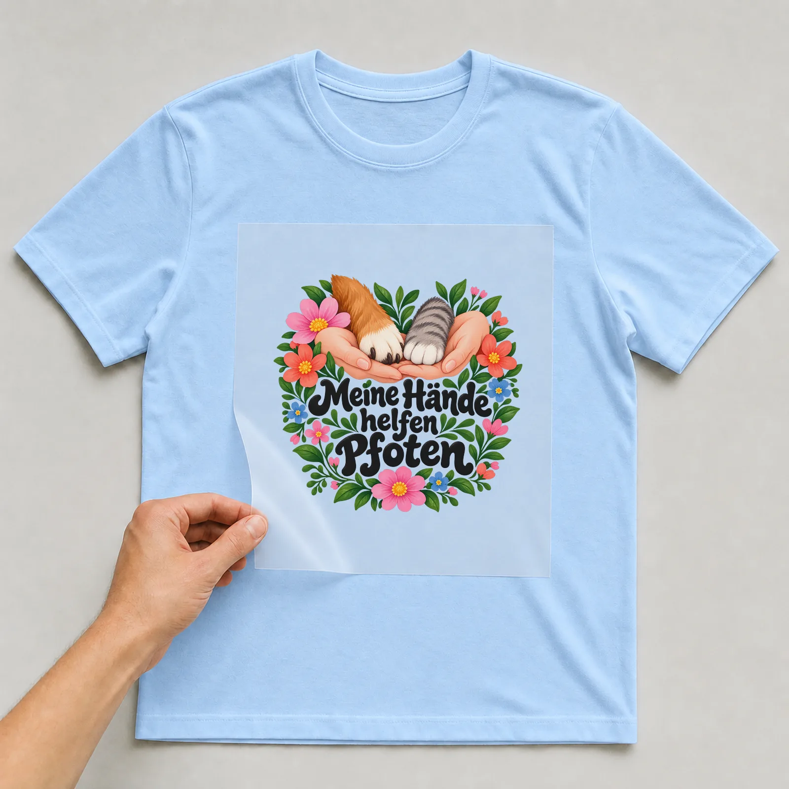 Bügelbild „Meine Hände helfen Pfoten“ auf hellblauem T-Shirt, Folie wird aufgelegt