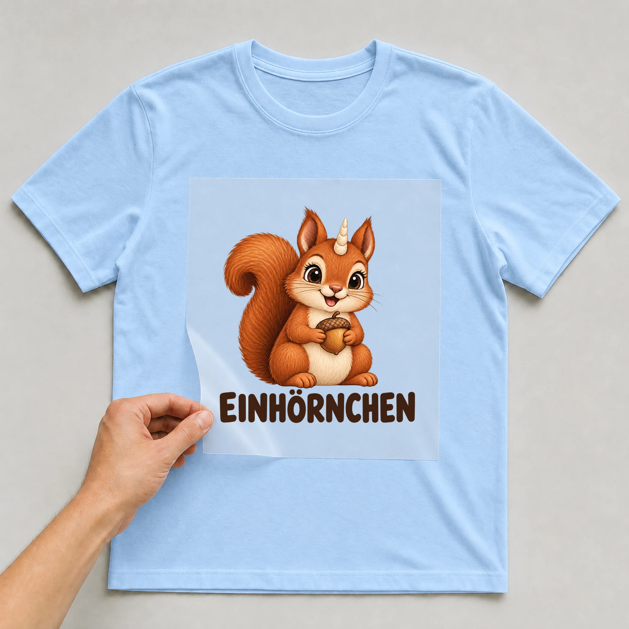 Bügelbild „Einhörnchen“ auf babyblauem T-Shirt, Folie wird aufgelegt
