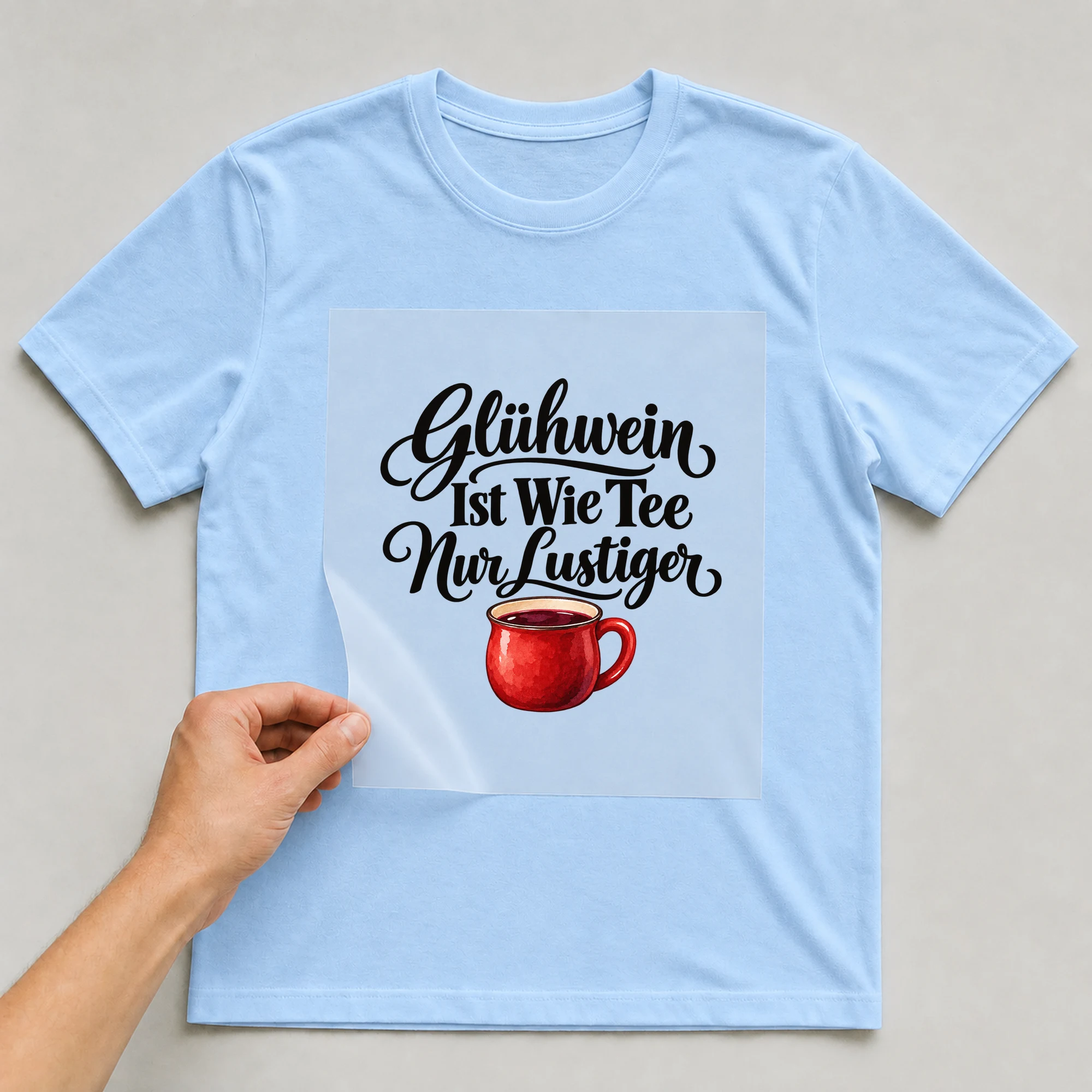 Bügelbild „Glühwein ist wie Tee nur lustiger“ auf babyblauem T-Shirt, Folie wird aufgelegt