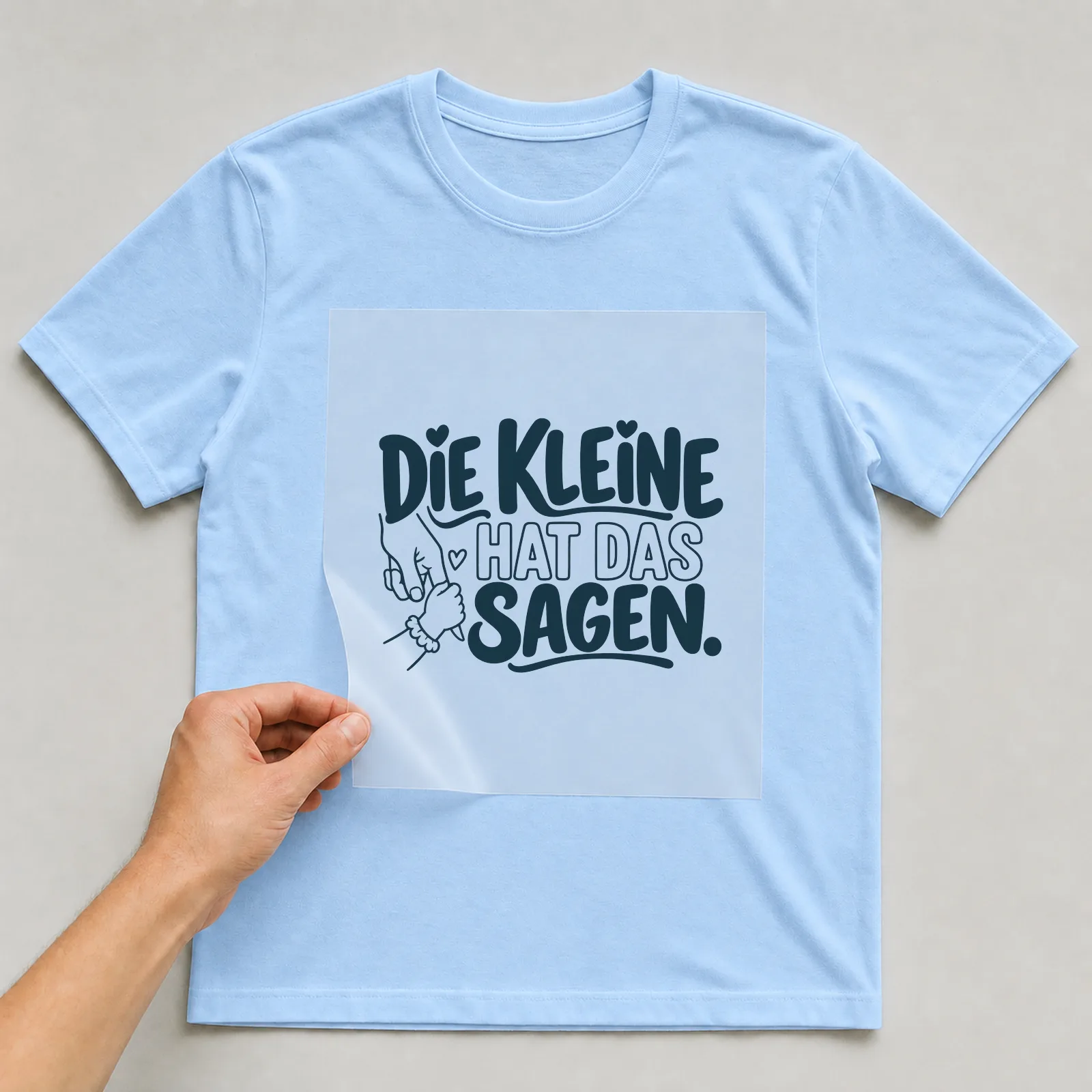 Bügelbild „Die Kleine hat das sagen“ auf hellblauem T-Shirt, Folie wird aufgelegt